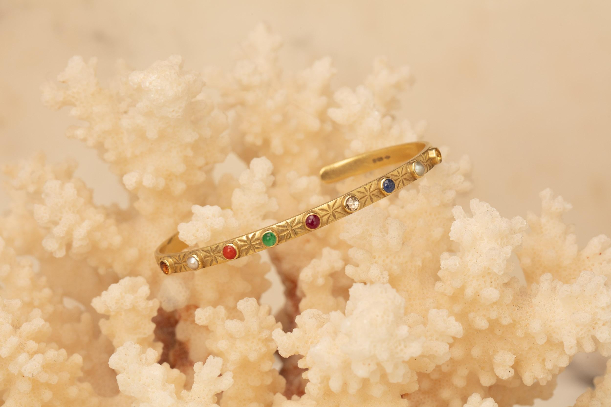 This piece holds nine cabochon gems set in an 18 karat gold cuff with engravings of stars and moons along the outer surface. The inner surface of the bangle is engraved with 