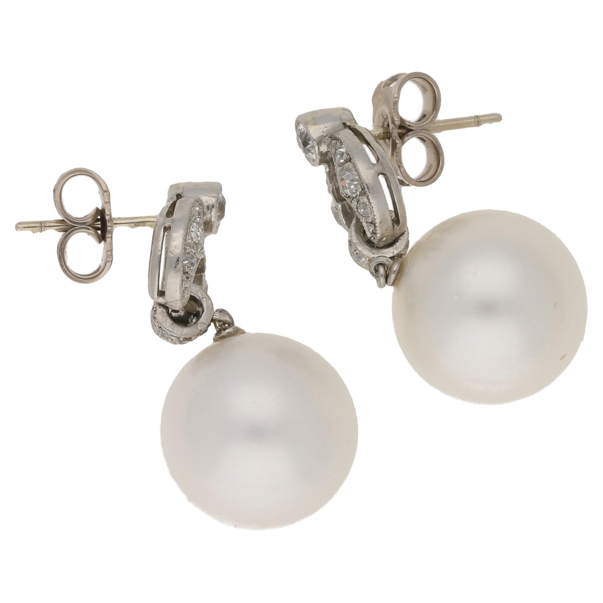 An elegant pair of 12mm South Sea Akoya pearl earrings. Topped with a full pave set articulated ring, connecting to a pierced openwork pannel of pave set Old European cut diamonds, topped with a collet set Old European cut diamond hiding the post