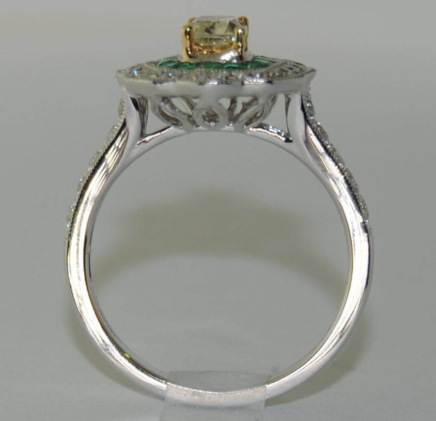 This ring features Cushion Center Fancy Diamond/Yellow and Round White Diamonds total 0.93 Carat weight, with small Emeralds weighing 0.46 Carat.  Mounted in 18 Karat White Gold, Size 6.25  