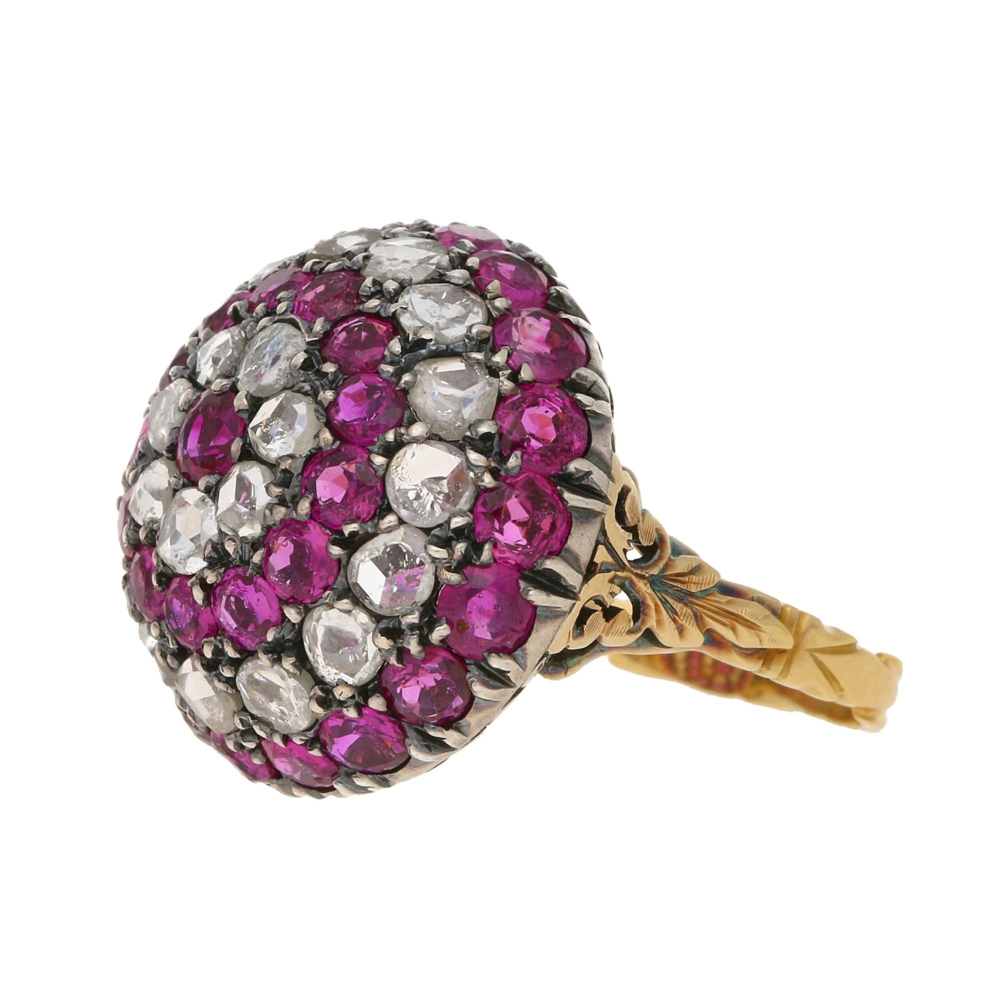 A Late Georgian style bombe cocktail ring claw set with thirty three Burmese rubies and twenty two rose-cut diamonds set in silver on gold. The underside of the ring is adorned with an ornate pierced openwork undercarriage leading to a gold carved