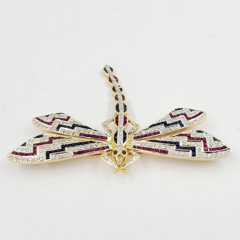 18 Karat White & Yellow Gold Dragonfly Pin Featuring Approximately 1.50 Carats of VS Clarity & H Color Diamonds, 1.50 Carats of Square Cut Rubies, & 1.50 Carats of Square Cut Sapphires. Length is 2 inches, and Width is 2.75 Inches. Finished Weight