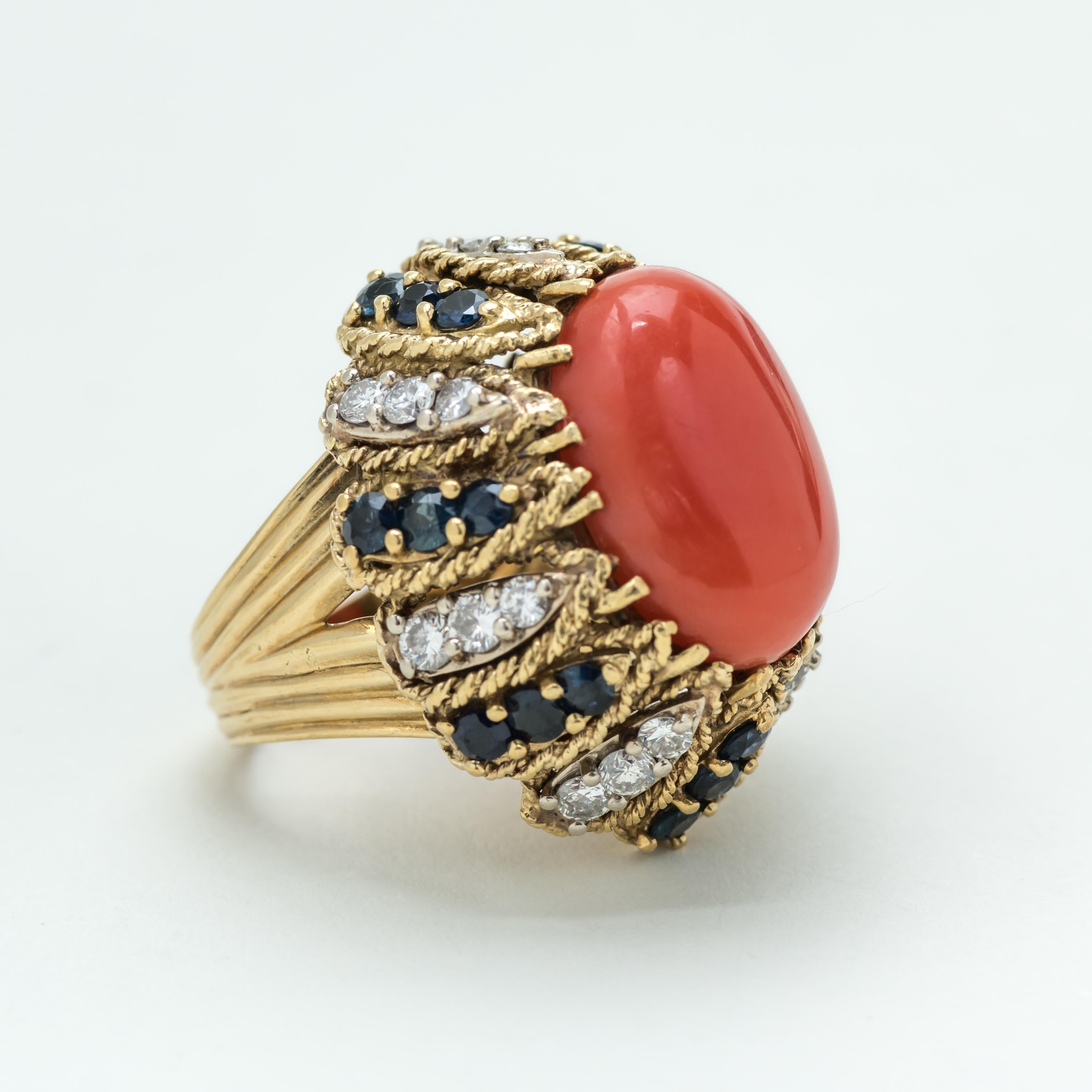 Italian 18 karat gold, diamond, sapphire ring with a prominent central Mediterranean Cabochon coral stone. The ring is exquisitely made. It has a striated band supporting the oval inset perimeter banding.

Size: 6 1/2