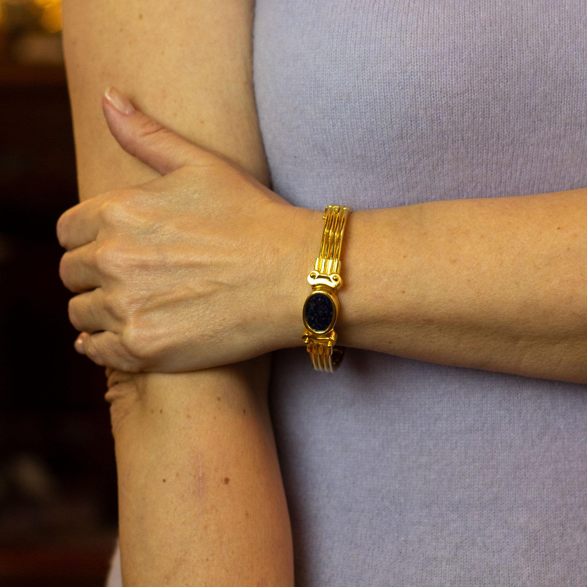 Ein Armreif aus 18 Karat Gelbgold in Form einer doppelendigen Säule mit einer ovalen Scheibe aus poliertem Lapislazuli. Der Armreif lässt sich seitlich mit einem Scharnierverschluss öffnen und wird mit einem Sicherheitsverschluss gehalten. Das aus