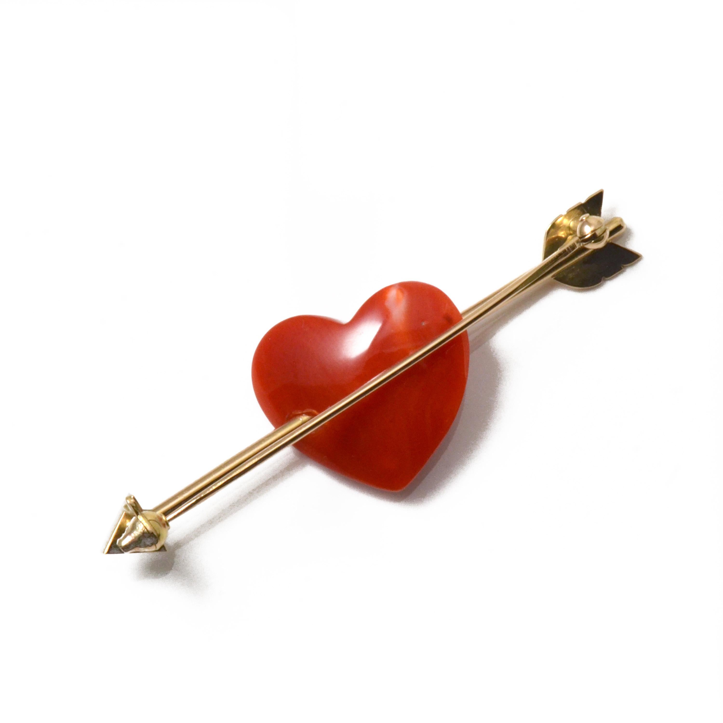 This is an 18 Karat Yellow Gold Heart Shaped Chiaka Sango (Oxblood Coral) Arrow Brooch with Diamonds. An 18 karat gold arrow pierces the Chiaka Sango (Oxblood Coral) heart, with three diamonds delicately set at the tip of the arrow. Matte and mirror