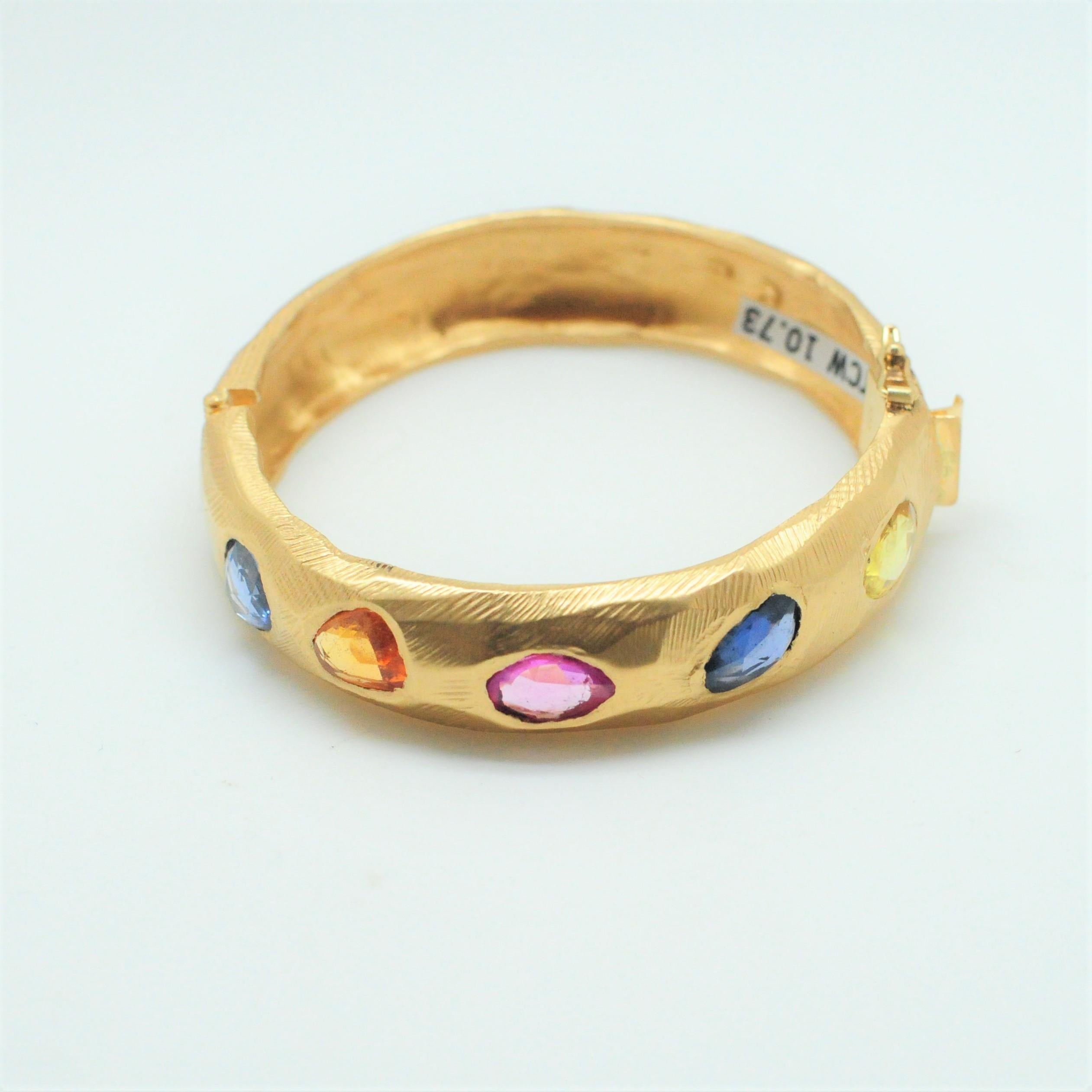 Handcarved 18KT Gold hinge bracelet with multi-colored sapphires including blue sapphires, orange sapphires, and pink sapphire.  One-of-a-kind bracelet with 10.73 total carats weight.  

Fits wrist size of 7.5-8.5