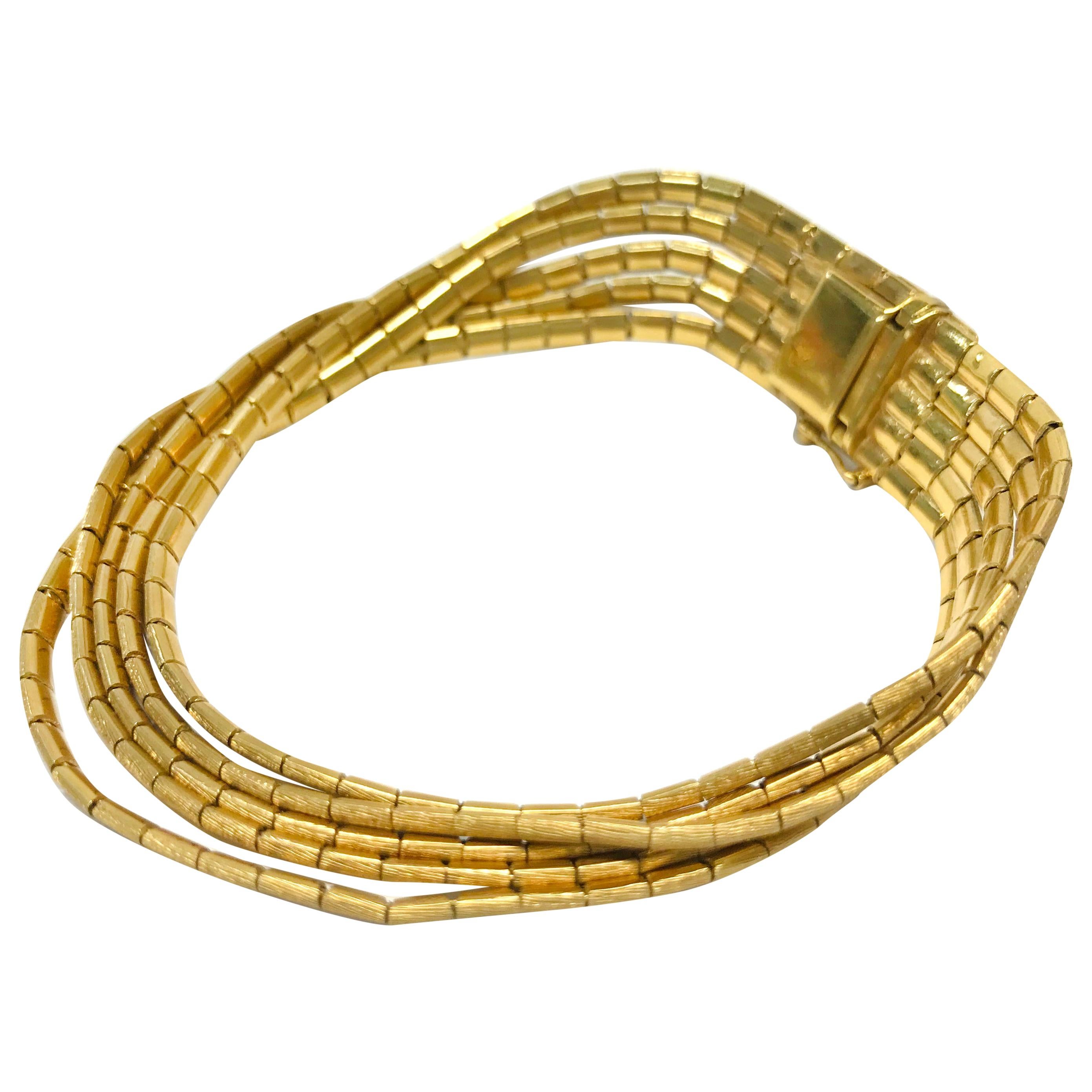 18K Gold Vintage Five-Strand Bracelet. This elegant bracelet showcases a large clasp that secures five strands of flowing gold threads, each composed of small rectangular links. The top features a Florentine finish, while the underside is smooth.