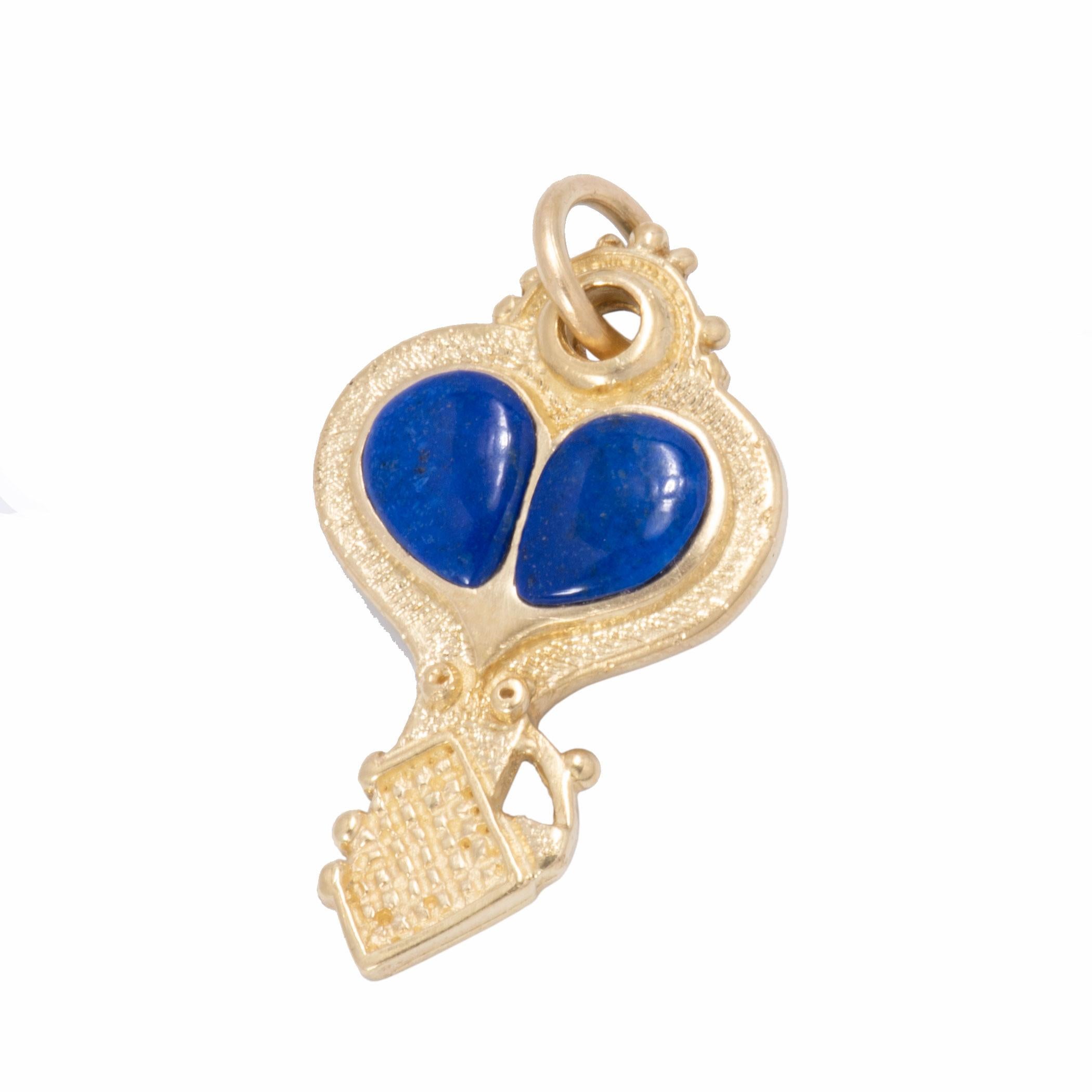 Lapis cabochons form the heart center of this 18 karat gold key and heart pendant. Both a stippled and satin finish, beading and a checkered relief at the tip of the key pendant draw focus to the heart shaped center. A token, a talisman, a memento