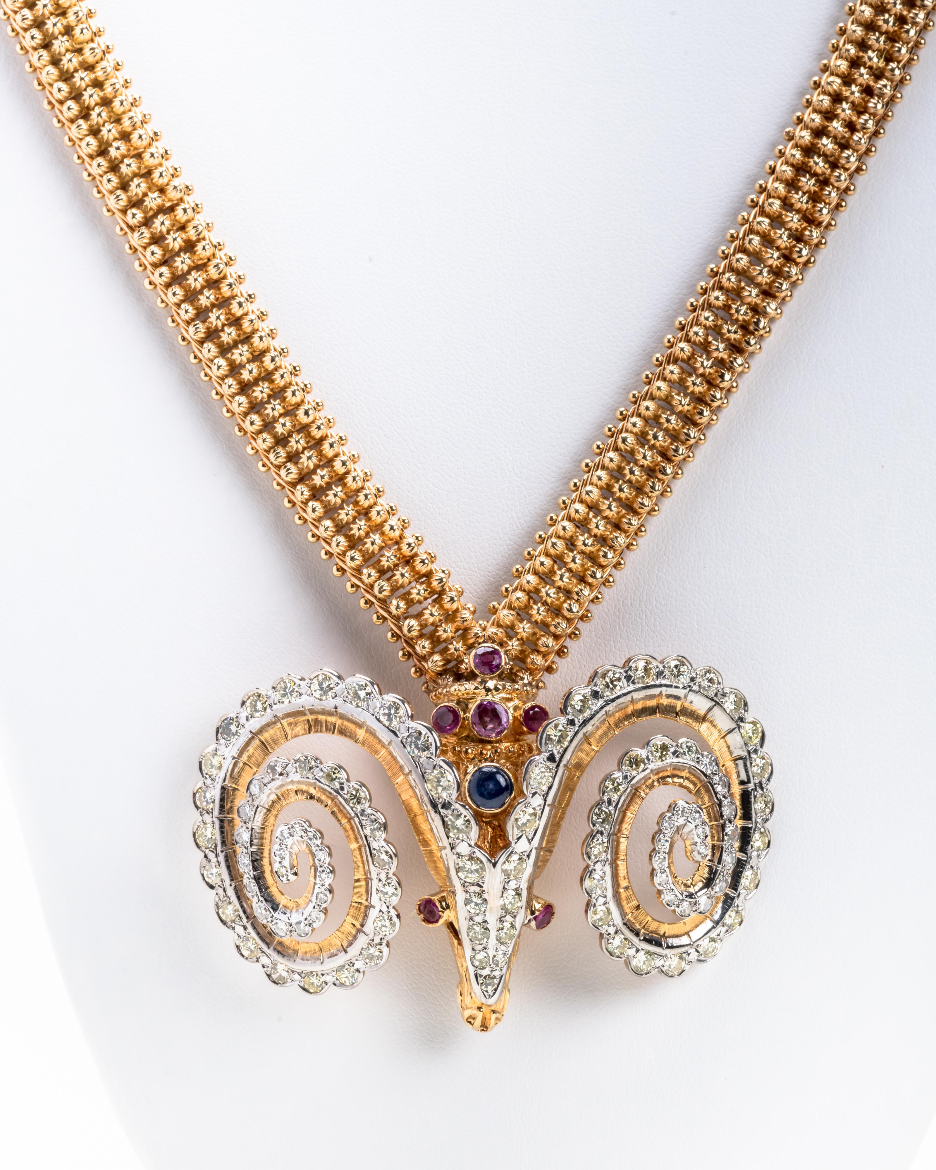 This beautiful 18 karat gold necklace has a highly stylized flexible chain and a prominent rams head pendant inset with diamonds, rubies and a Cabochon sapphire. The necklace is unique in it's design.

Size: L: 26