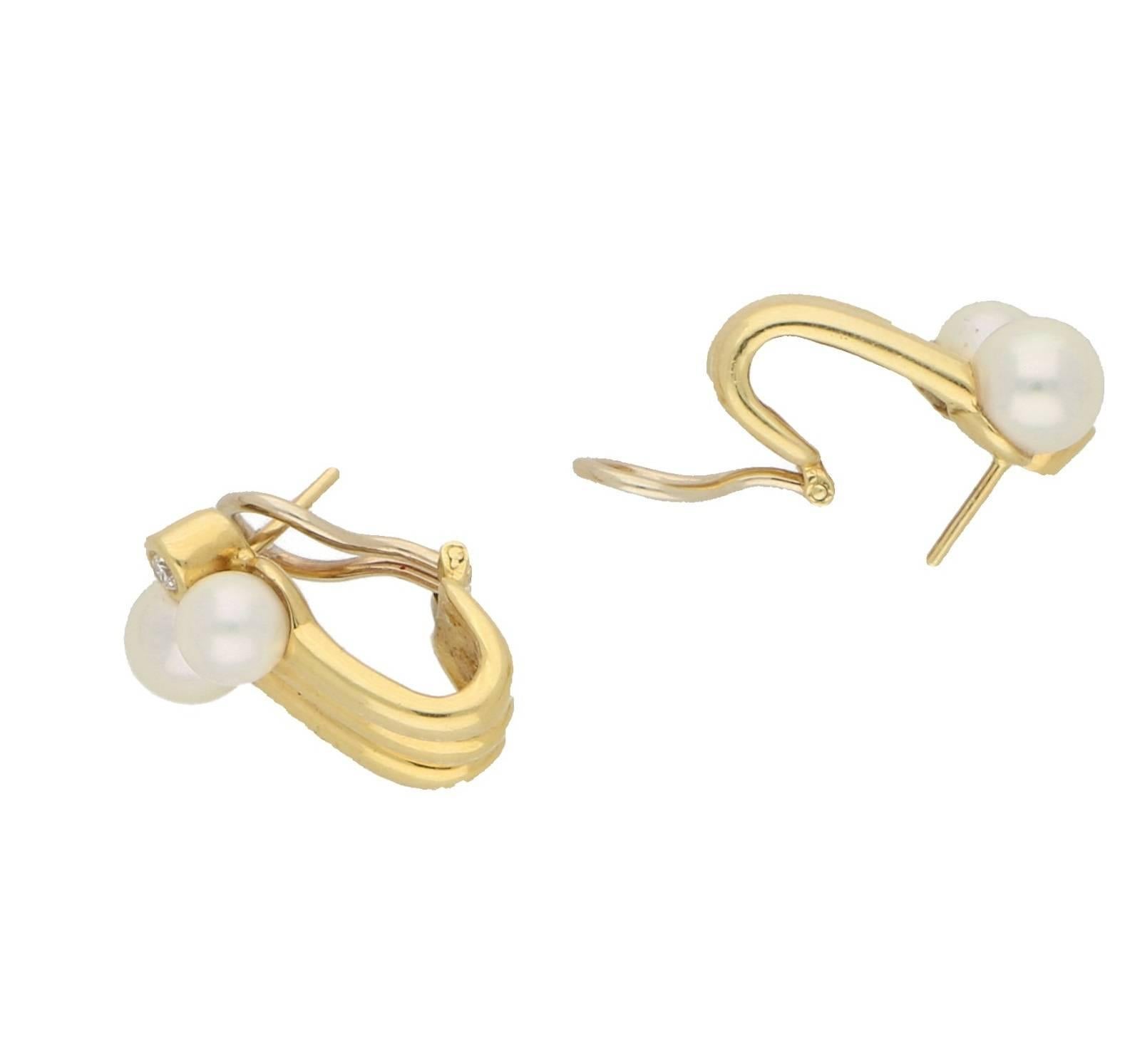 These stunning earrings comprise a round brilliant cut diamond in a rubover setting accented by two pearls that are set in three rows of 18kt yellow gold in a gas pipe design that curves under the post fitting. Total estimated diamond weight,
