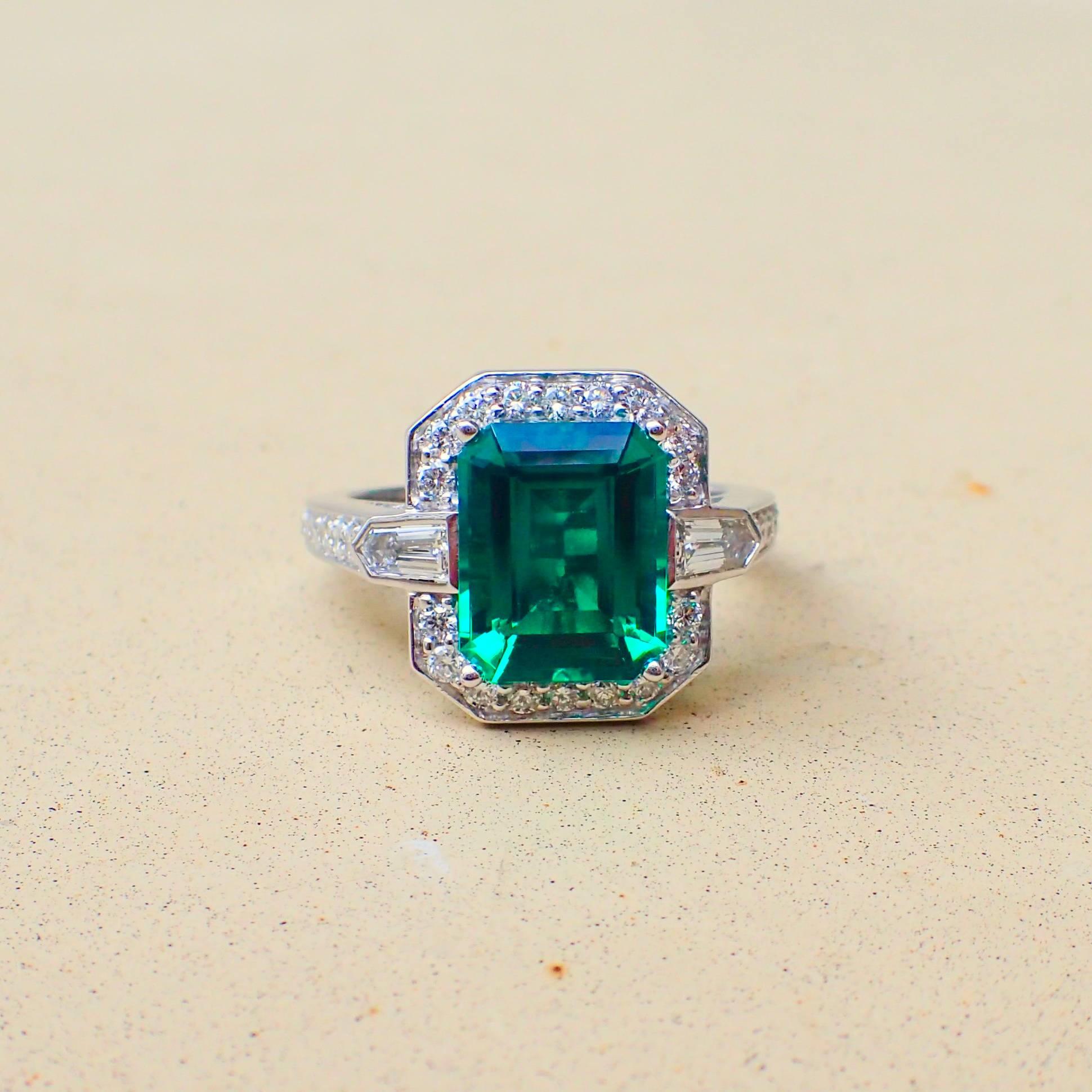 An 18k white gold ring is set with one (1) Emerald Cut Chatham-Created Emerald that measures 10.01mm x 8.01mm and weighs 2.83 carats with Clarity Grade VS-VVS and two (2) Bullet Cut Diamonds, one that measures 4.1mm x 2.3mm and weighs 0.14 carats