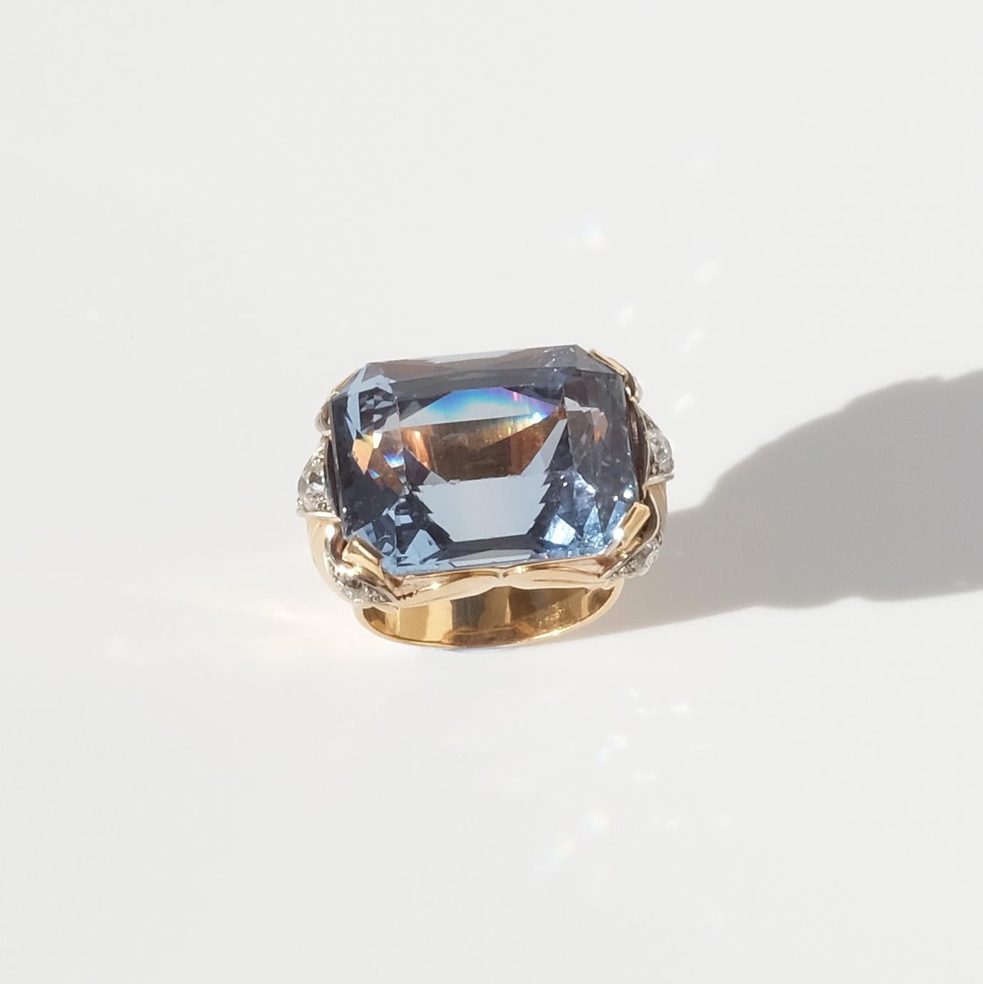 This 18 karat gold ring has a large clear-blue rectangular mixed-cut synhtetic spinel. The setting is adorned with six old-cut diamonds and beautiful gold decorations.

The unconventional very large size of this ring radiates powerfulness and