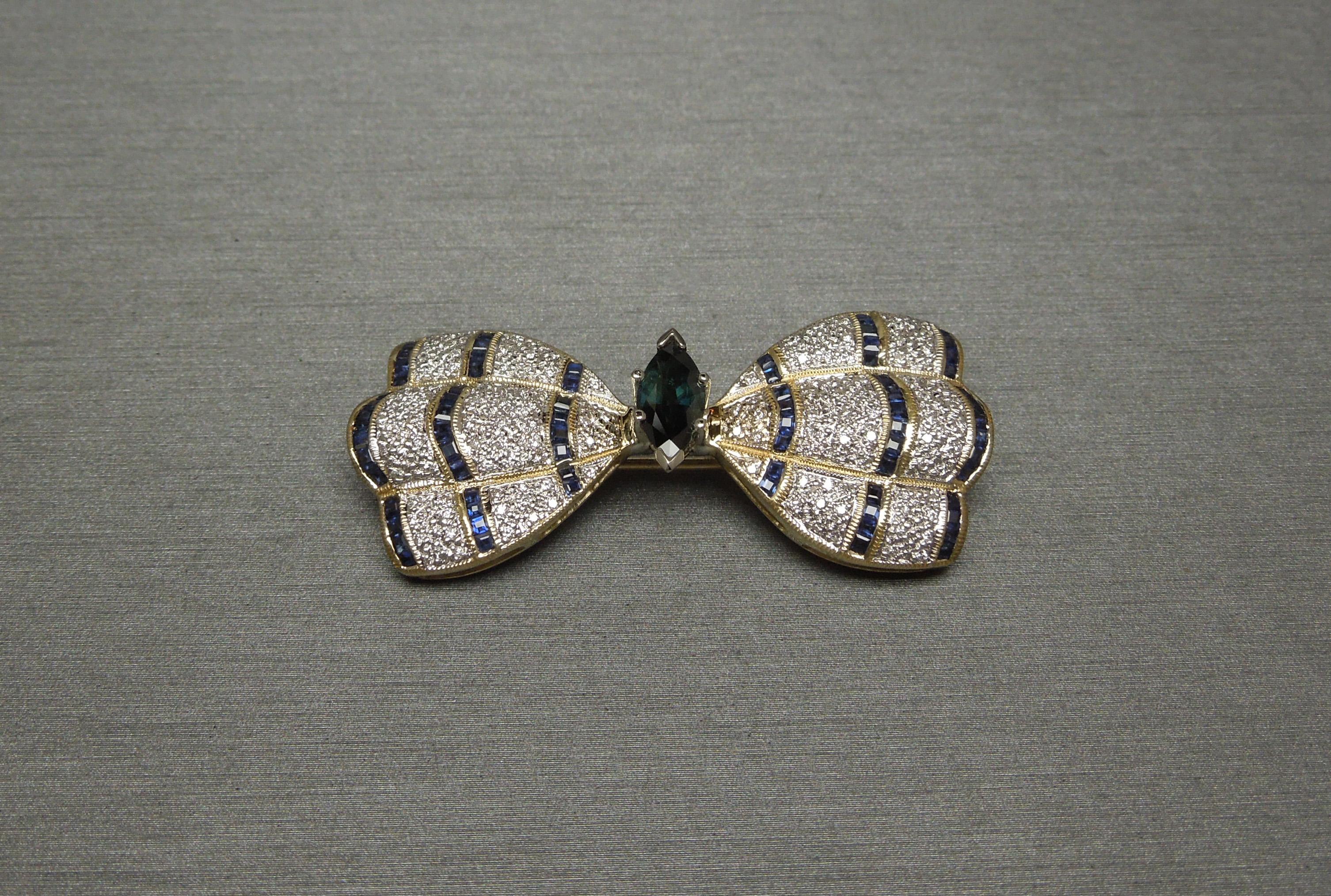 This 18 Karat Gold Sapphire & Diamond Butterfly features a central 1.20 carat Marquise cut Natural Color Changing [Blue-Green] Sapphire, resembling the body of Butterfly, at 10mm in length x 4.7mm in width, securely set in a 6-Prong White Gold head