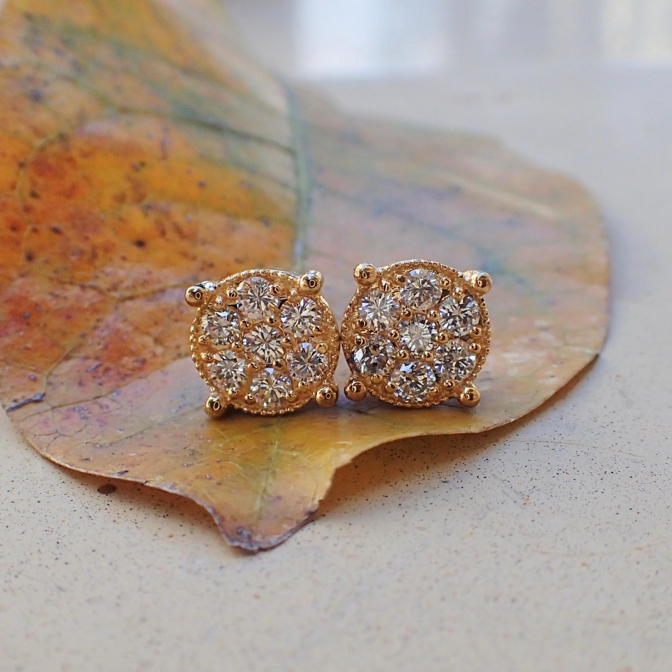 A pair of 18k yellow gold earrings are prong set with two (2) Round Brilliant Cut diamonds measuring 2.6mm x 2.6mm that weigh a total of 0.14 carats with Cold Grade H and Clarity Grade VS-SI and surrounding the center stones are twelve (12) prong