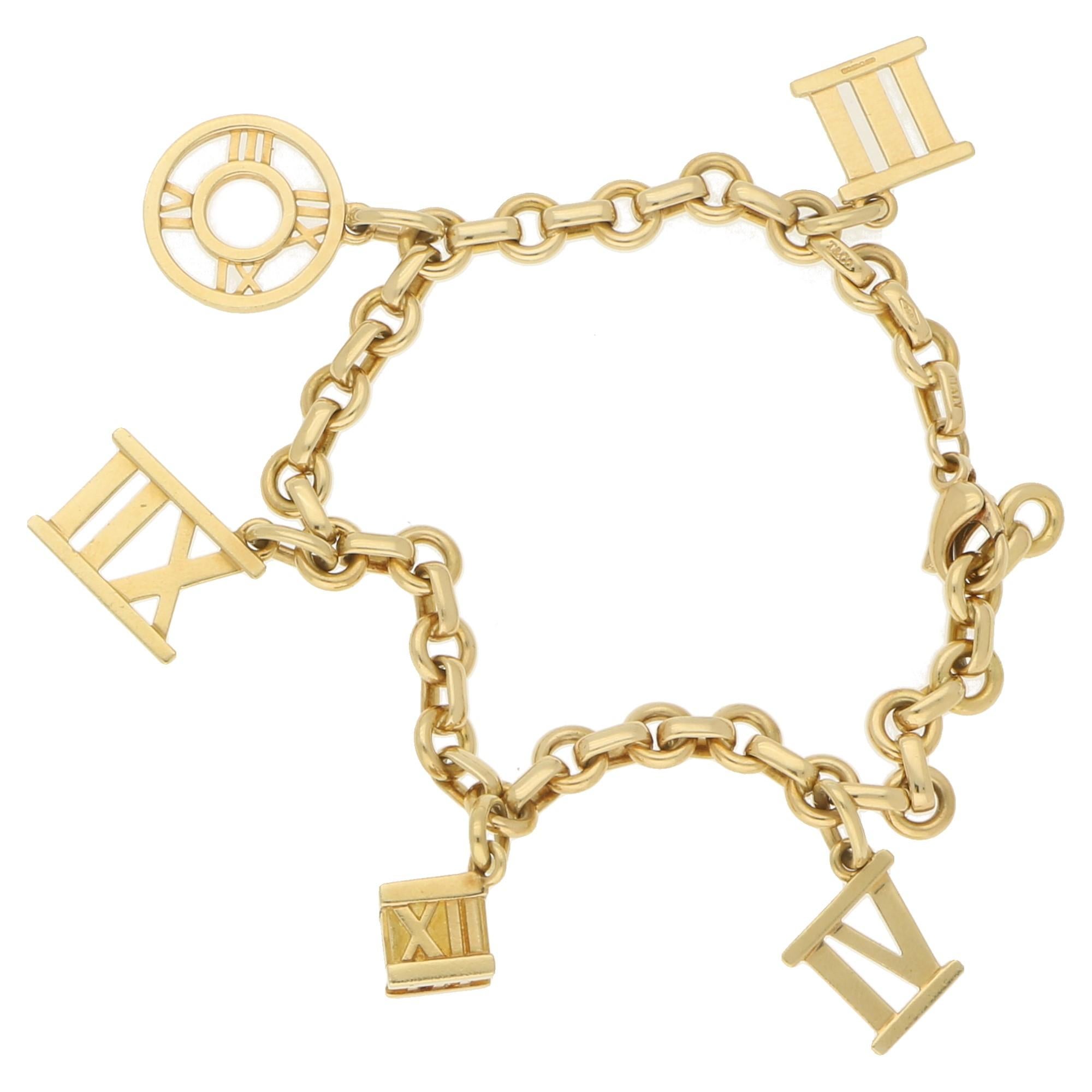 A fine vintage charm bracelet by Tiffany & Co. from their Atlas collection. It is well crafted from solid 18k yellow gold in a fine polished finish and carries five Roman numeral charms, also a cube charm and a round charm. The piece fastens with a