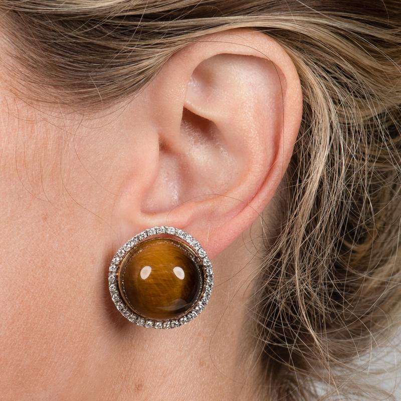 These beautiful and unique earrings feature Tiger's eye cabochon accented by a halo of round diamonds totaling approximately 1.28 carats total. They are set in 18 karat yellow and white gold with a small ruby inset on the back of each earring. Omega