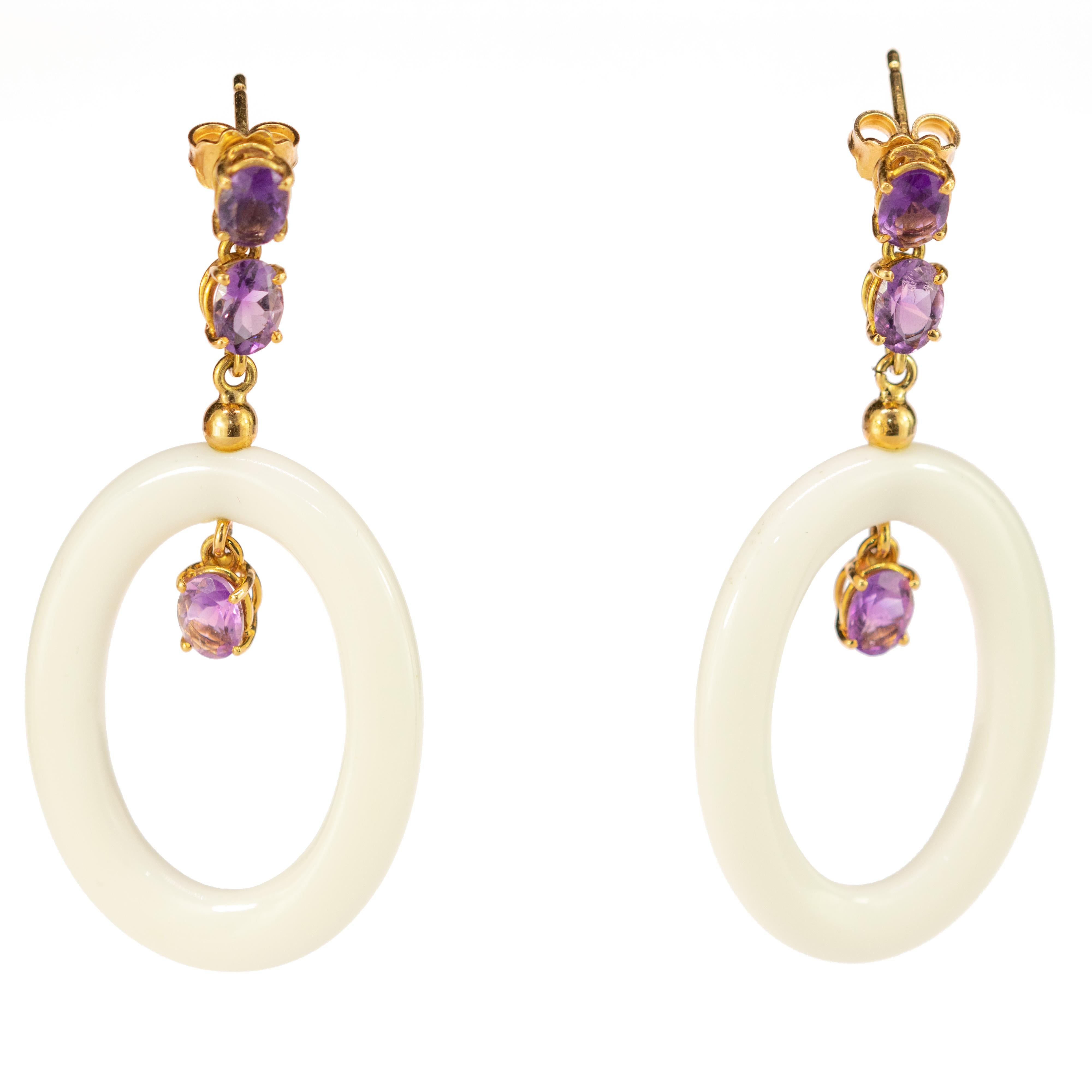 An enchanted oval white agate donut-shaped earrings holded by an 18k yellow gold delicate chain with two beautiful amethyst on top followed by a gold round gem and a third amethyst holding inside the agate. Modern designs full of details and soft