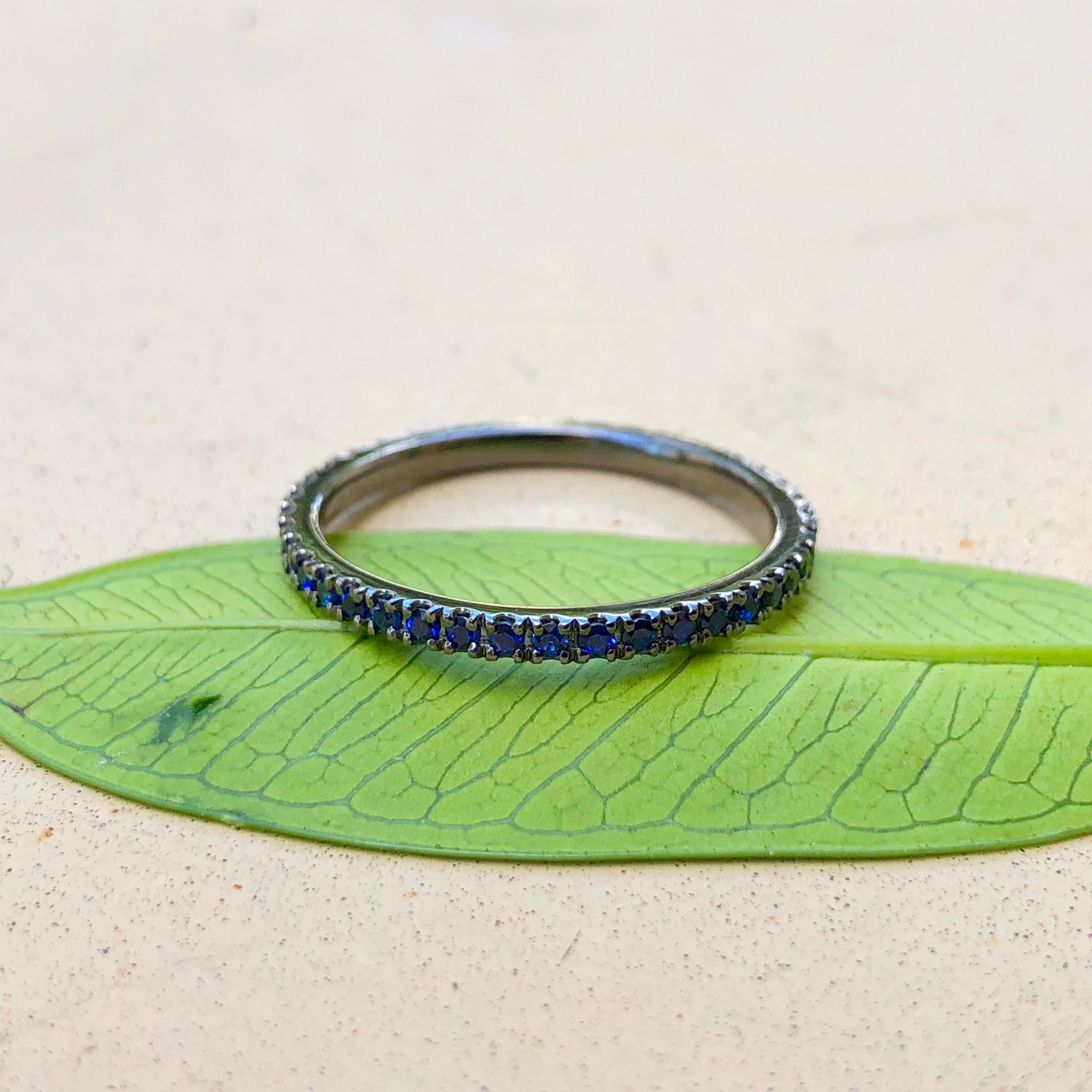 An 18k white gold eternity band with black rhodium plating is set with with thirty-six (36) Round Brilliant Cut Chatham Sapphire that measure 1.3mm a 1.3mm. The ring is a size 6.5 and weighs 1.6 grams (1 pennyweight).

At By Design Jewelers, our