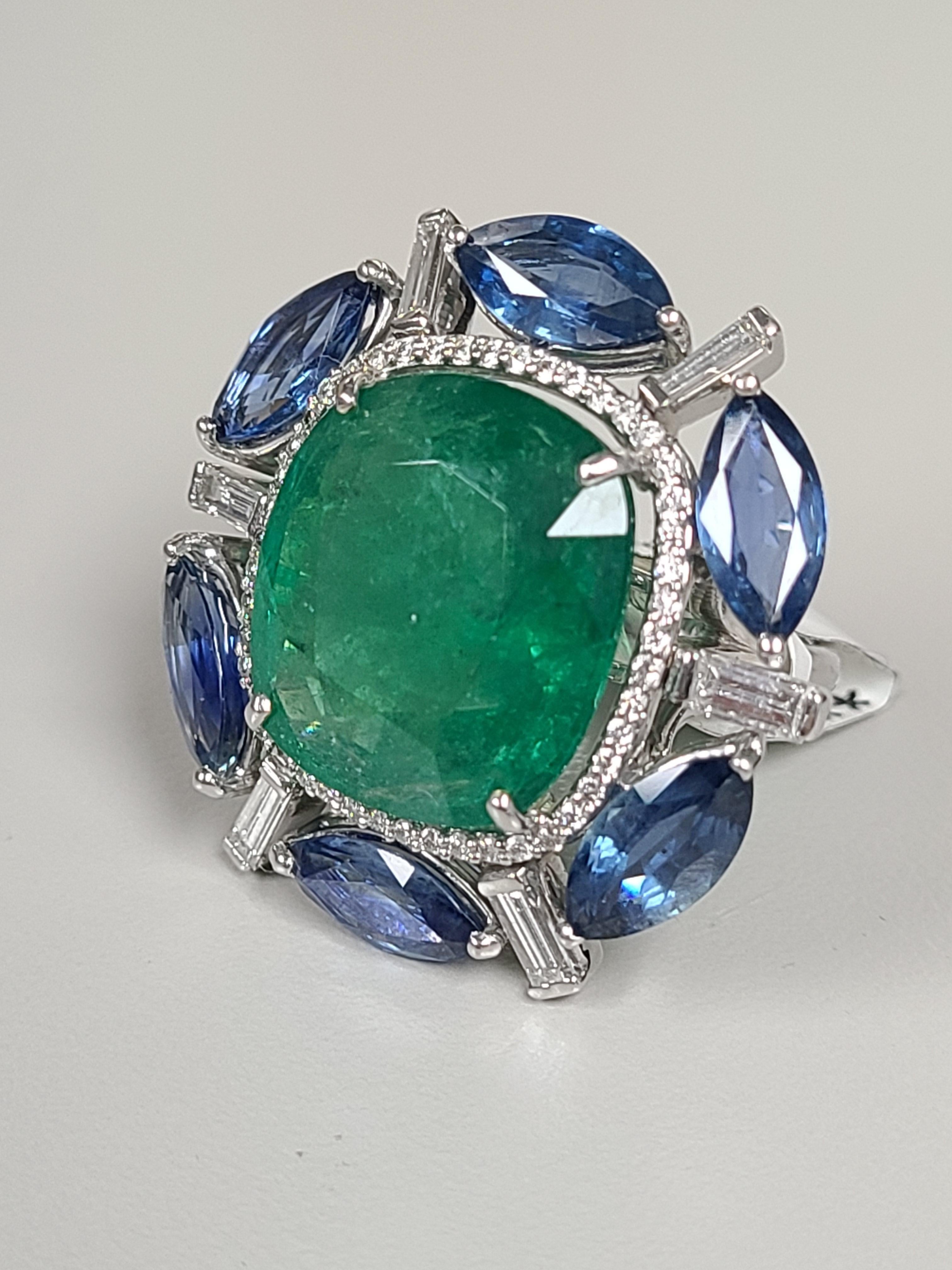 A gorgeous Zambian Emerald & Ceylon Blue Sapphire cocktail ring set in 18K Gold and Diamonds. The Emerald is completely natural, without any treatment, and originates from Zambia. The weight of the Emerald is 14.54 carats. The weight of the Blue