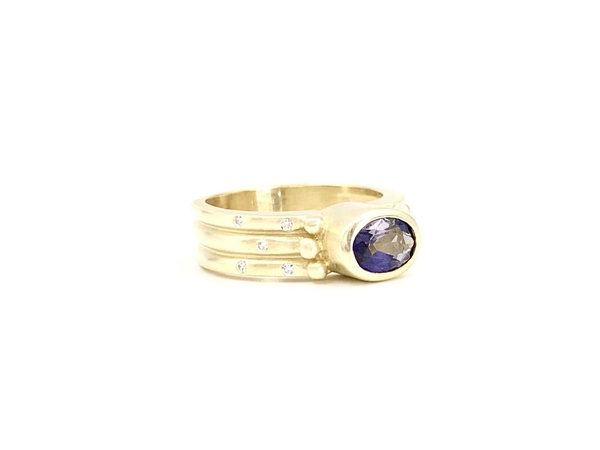 A well made and wearable 6.5mm wide 18 karat yellow gold oval purple iolite ring accented with .10 carats of round brilliant burnished diamonds. Diamond quality is approximately G color, VS2 clarity. Yellow gold has a beautiful, rich satin finish