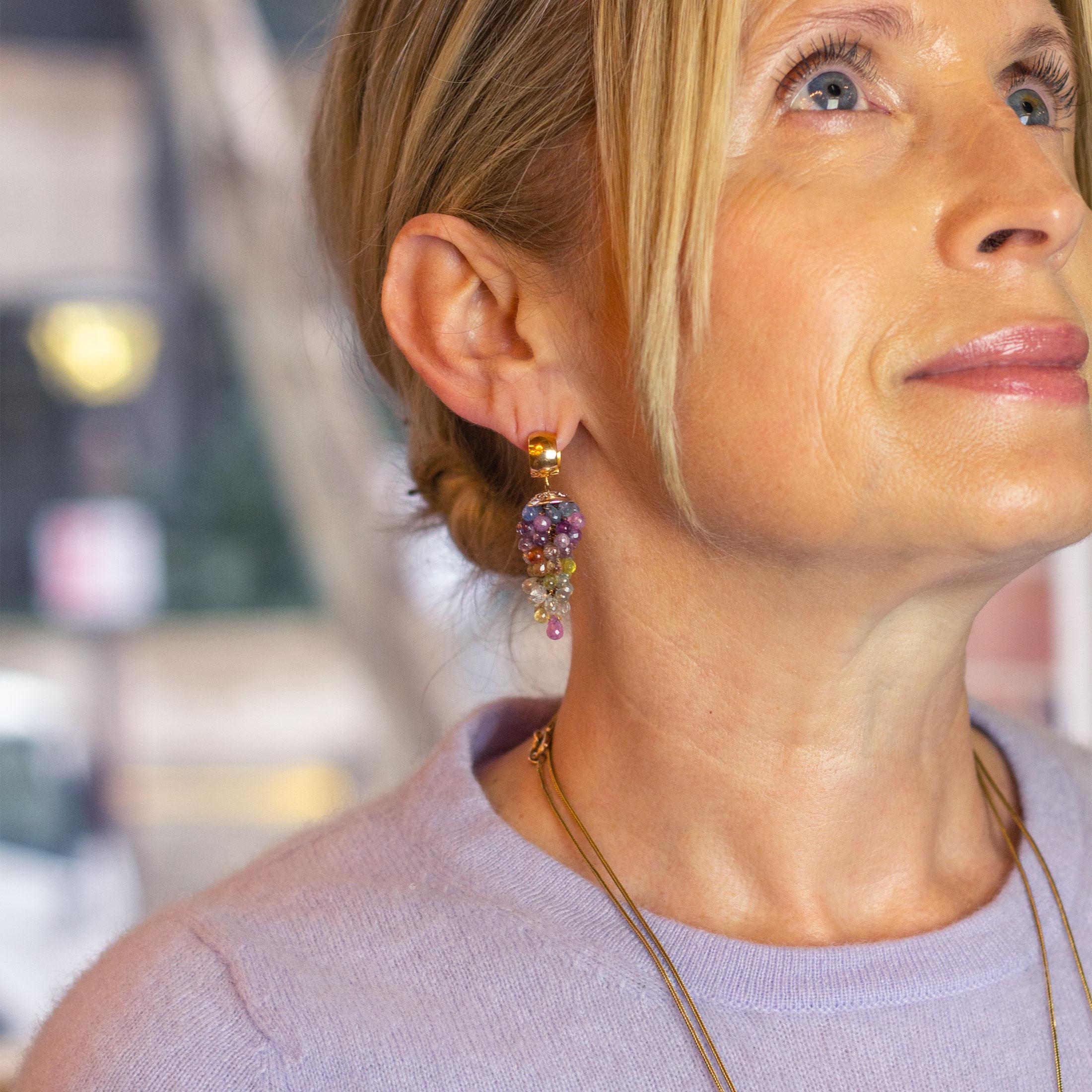 A pair of unusual 18 karat rose gold earrings set with clusters of briolette sapphires. The clasp of the earrings are rose gold huggies to which attaches a pierced white gold disc housing a drop of multicoloured briolette sapphires in a grape style