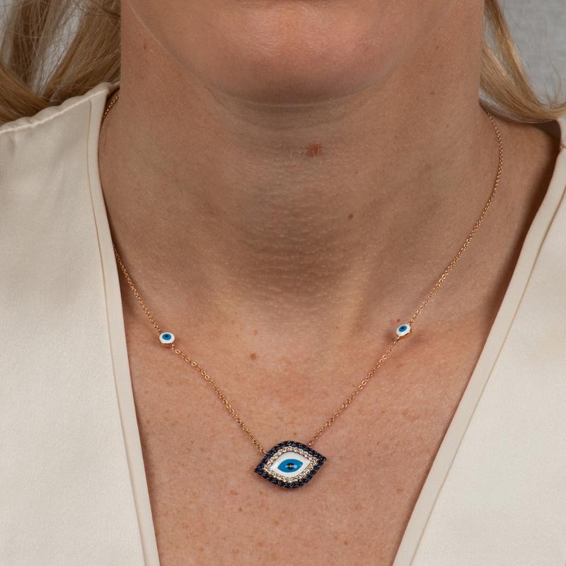 Protect yourself by wearing this pendant necklace featuring an enamel evil eye surrounded by 0.22 carat total weight in round diamonds and 0.45 carat total weight in blue sapphires set in 18 karat rose gold. The 16