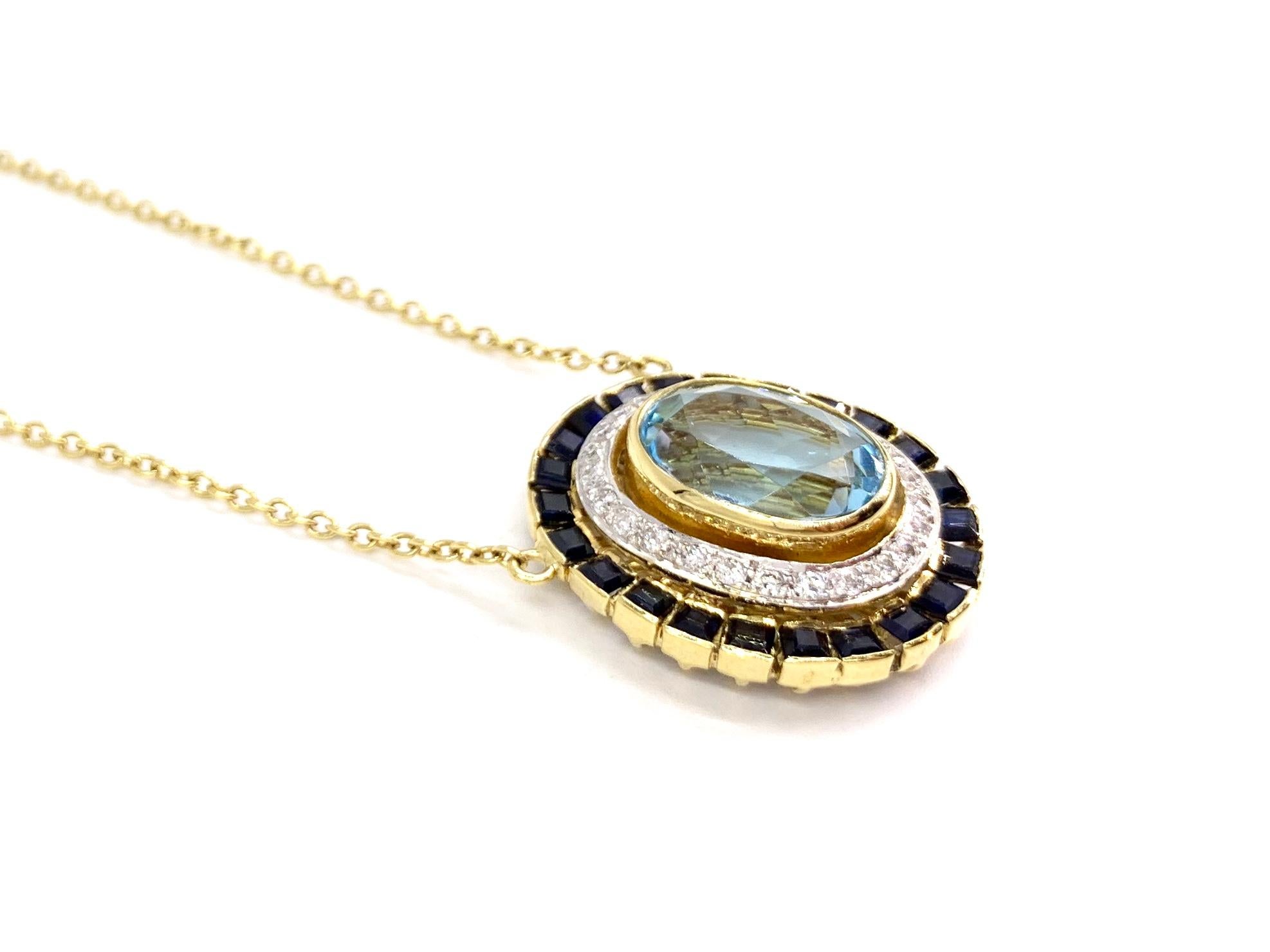 A fashionable 18 karat yellow gold stationary pendant necklace featuring a faceted oval sky blue topaz gemstone surrounded by approximately .26 carats of white diamonds and 2.50 carats of princess cut dark blue sapphires. Diamond quality is