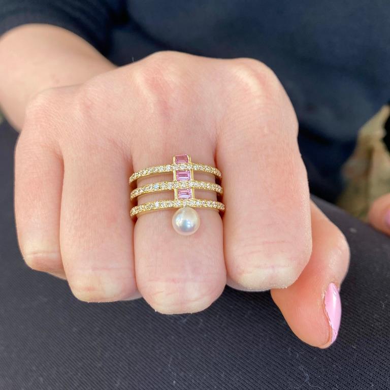A bold and modern piece, this 18 Karat gold ring combines a mix of diamonds with pink sapphire baguettes.  Edging the ring is a chunky white pearl 
Materials: 18 Karat Gold, 1mm Diamonds (1.00ct), 3 x 2mm pink Sapphire Baguettes, 5mm white Akoya