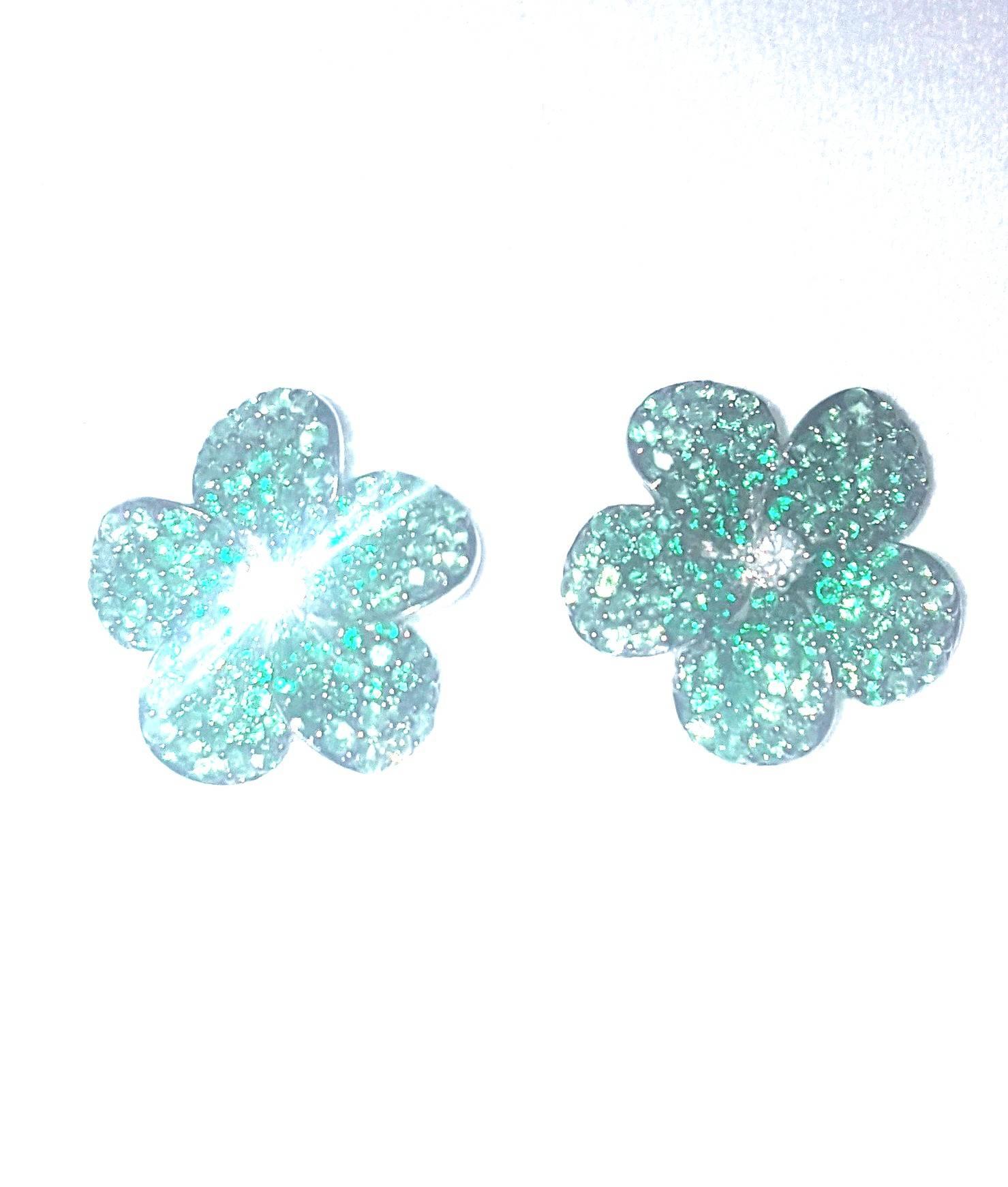 Nature motifs have been a jewelry design staple for centuries.  These stunningly tailored pierced earrings depict a five petal flower encrusted in green tsavorites.  A four prong set round white diamond centers each flower.  Tsavorites have a