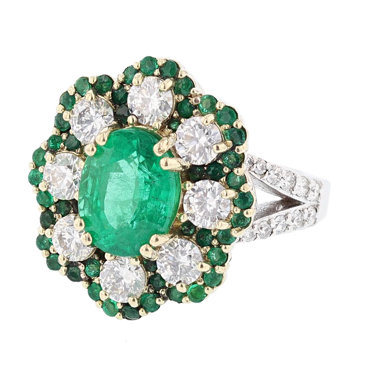 This ring is made in 18 karat white and yellow gold and features a 2.66ct oval cut emerald. The ring also features a diamond halo with 8 round cut diamonds, prong set weighing 1.51cts; and 48 round cut emeralds, prong set weighing 0.68cts; and a