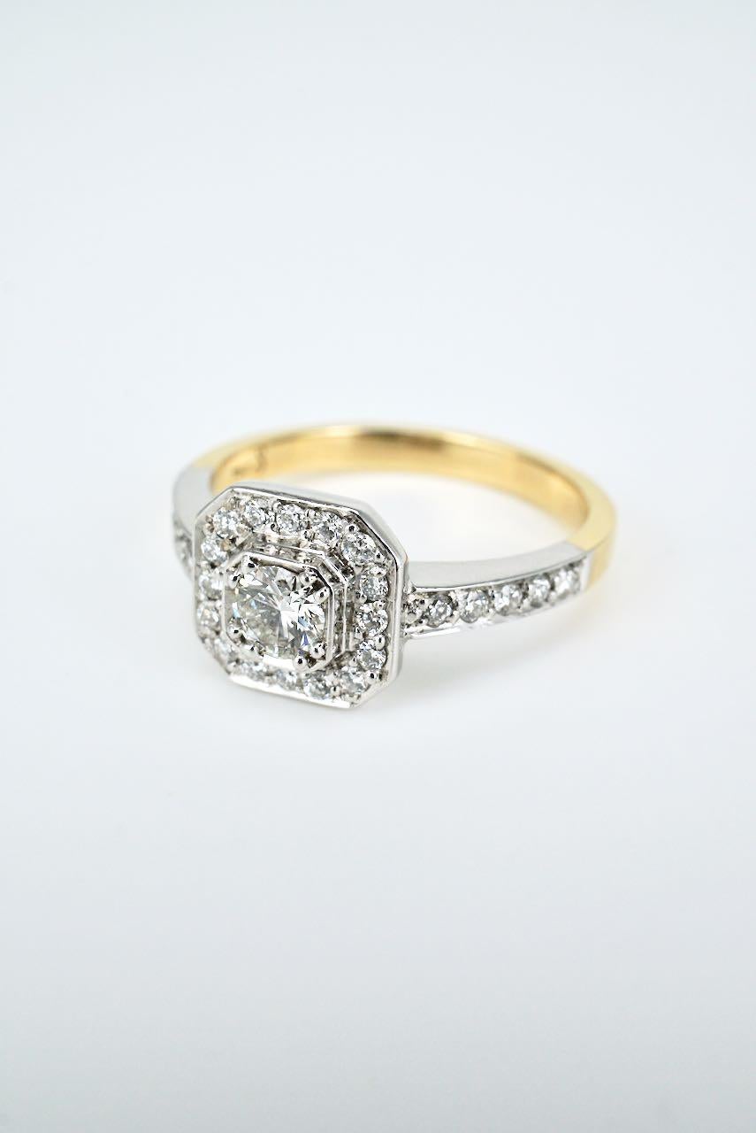 An Art Deco style ring featuring a central round brilliant cut diamond bead set in 18k white gold within an octagonal border of 16 diamonds and a further five diamonds down each shoulder on a yellow gold shank - this classic ring captures the