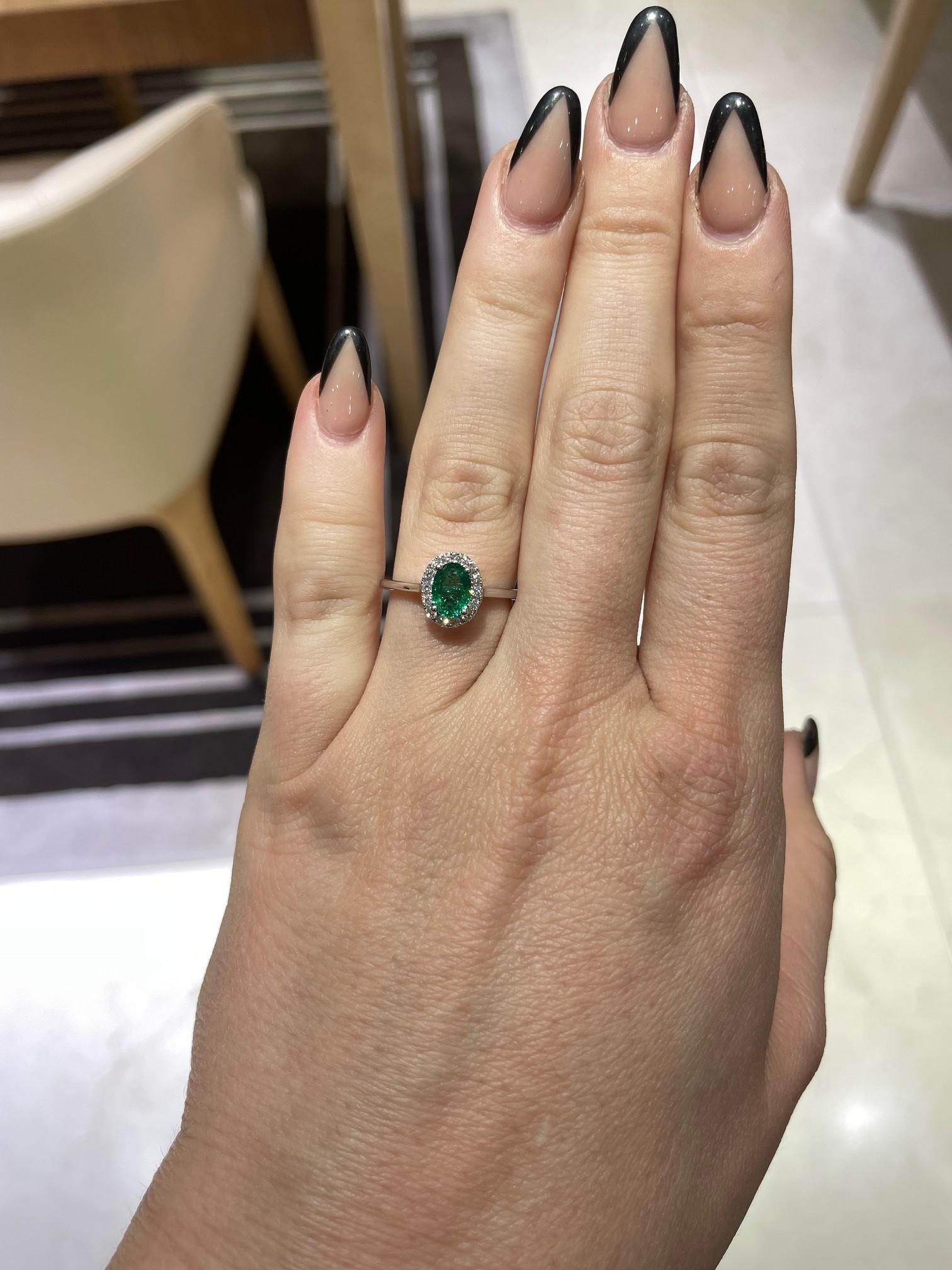 This elegant ring is crafted of 18 karat white gold with a center oval Zambia green emerald totaling 0.65 carats and is surrounded by 14 round brilliant cut diamonds totaling 0.17 carat total weight with G-H color and VS2-SI1 clarity.