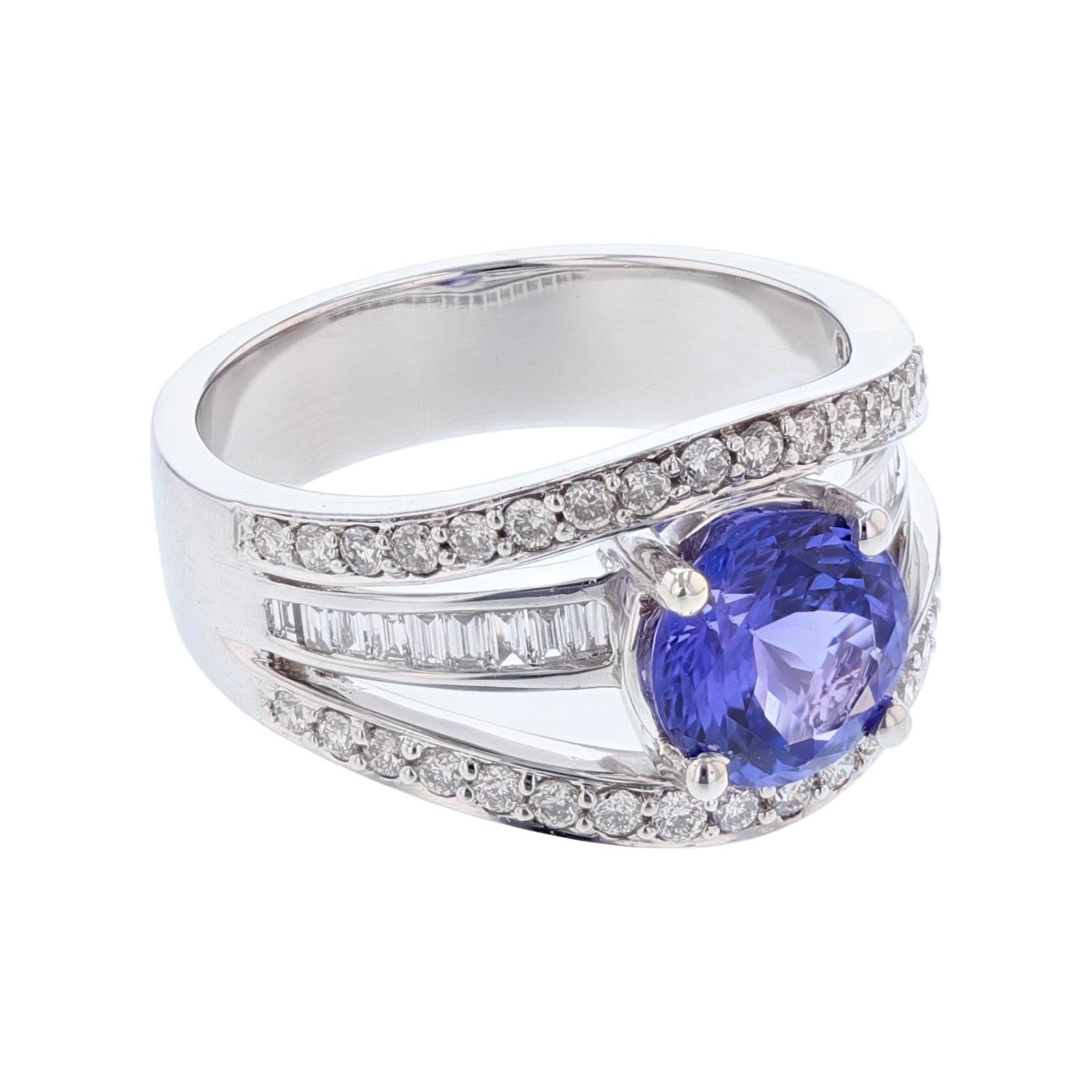 This ring is made in 18 karat white gold. The center stone is an round cut tanzanite weighing 1.82 carats and is prong set. The mounting features 36 round cut, prong set diamonds weighing 0.46 carats and 18 baguette cut diamonds weighing 0.23 carats