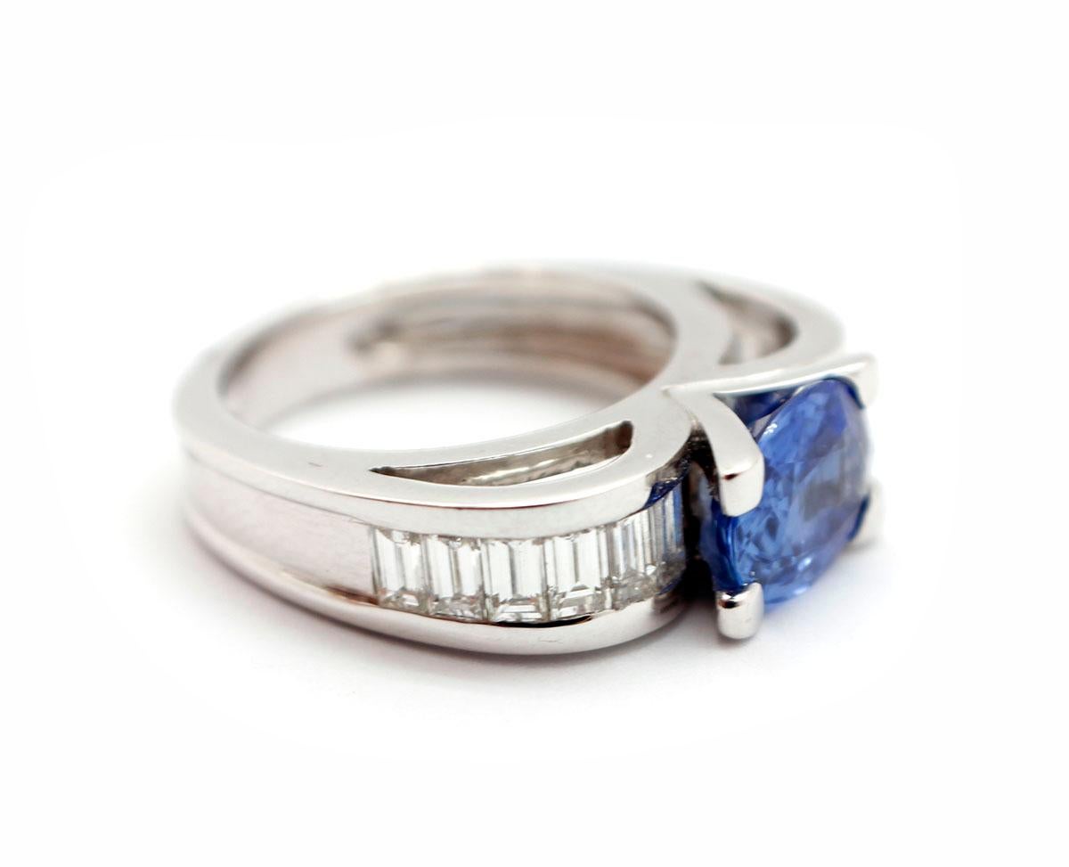This contemporary fashion ring is made in solid 18k white gold. It holds an oval-cut sapphire at its center weighing approximately 2.50 carats. The sapphire is accented by baguette-cut diamonds for an additional weight of 0.72ct. The ring measures