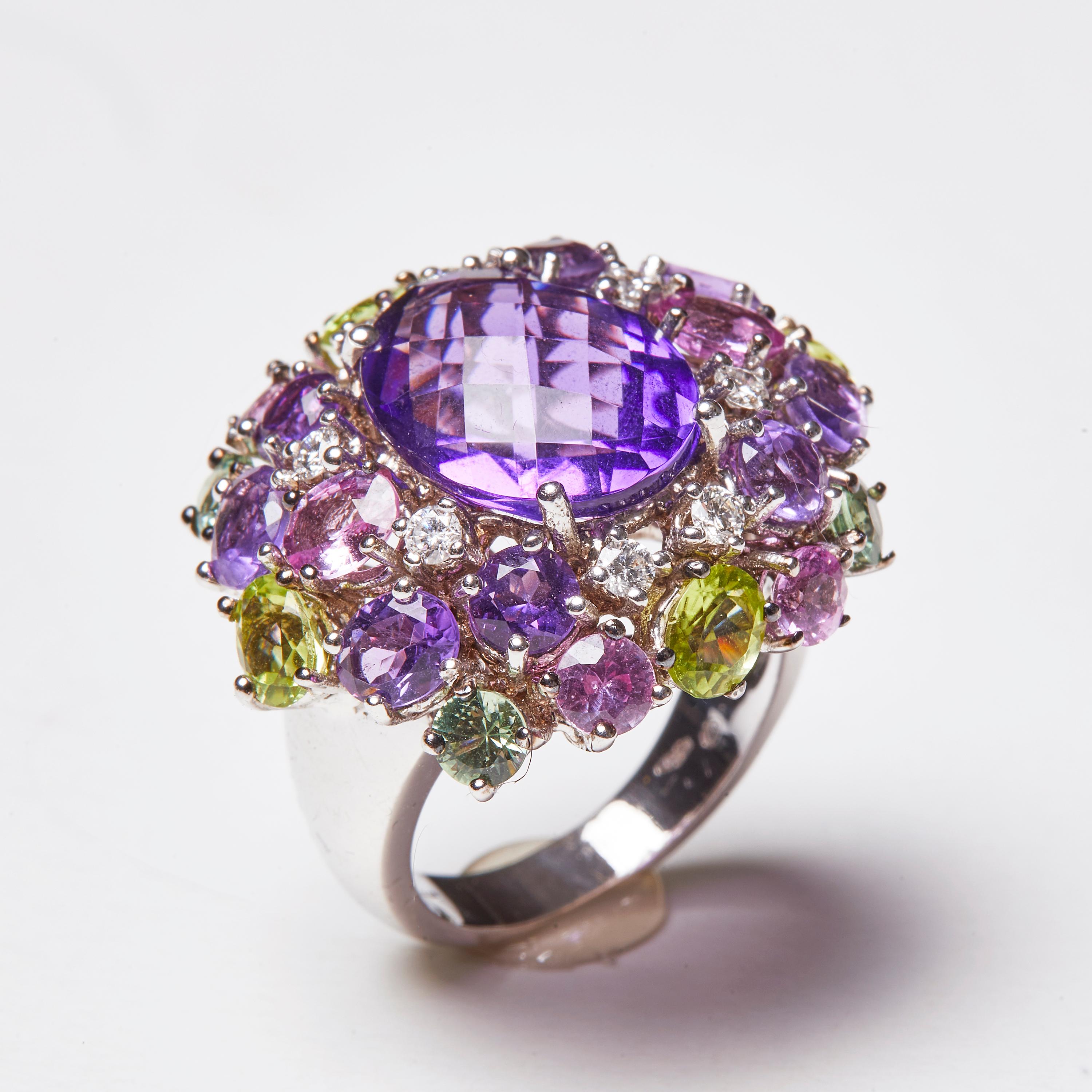 Dieser wunderschöne 18 Karat Weißgold Amethyst-Diamanten und Multi-Color-Cocktail-Ring verfügt über einen wunderschönen Amethyst-Mittelstein im Ovalschliff, umgeben von einer Vielzahl von farbigen Edelsteinen und Diamanten. Die Steine sind