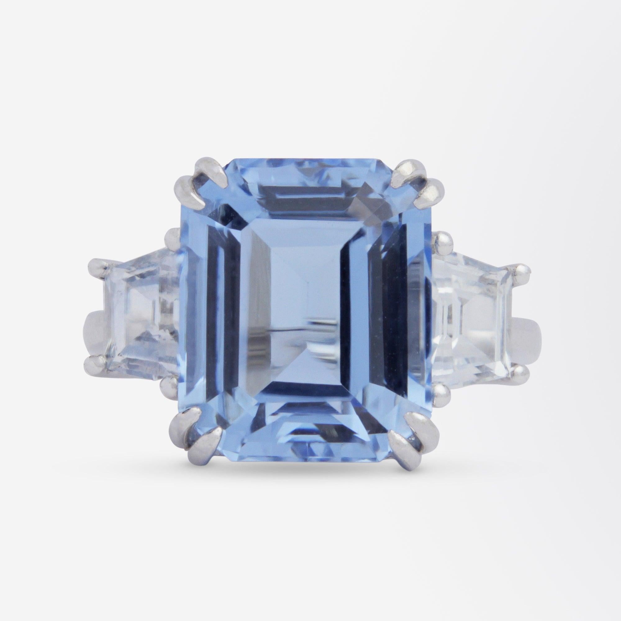 An excellent aquamarine and white sapphire cocktail ring set in 18 karat white gold. The ring centres on a 7.05 carat emerald cut aquamarine which is 'bright mid blue' and 'eye clean'. The shoulders of the ring are each set with a single white (or