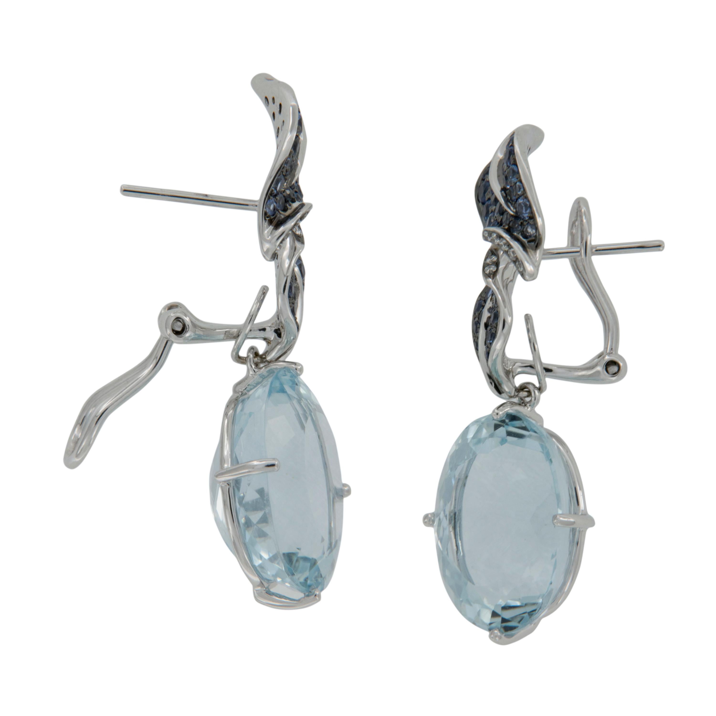 Crafted in fine 18 karat white gold these lovely dangle earrings showcase 20.98 Cttw. gem quality aquamarines, hanging from earthy designed leaves accented with beautiful blue sapphires which sets off the Aquamarine's perfectly! Earrings have posts