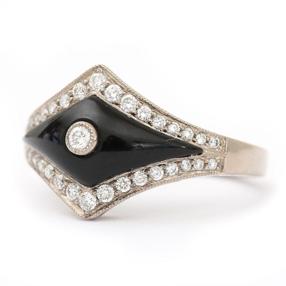 An 18 karat white gold onyx and diamond ring designed in the Art Deco style. This ring has a domed elongated diamond shape onyx section set with a 0.03 diamond in the centre. It has 34 diamonds surrounding the onyx set in 18k white gold, making an