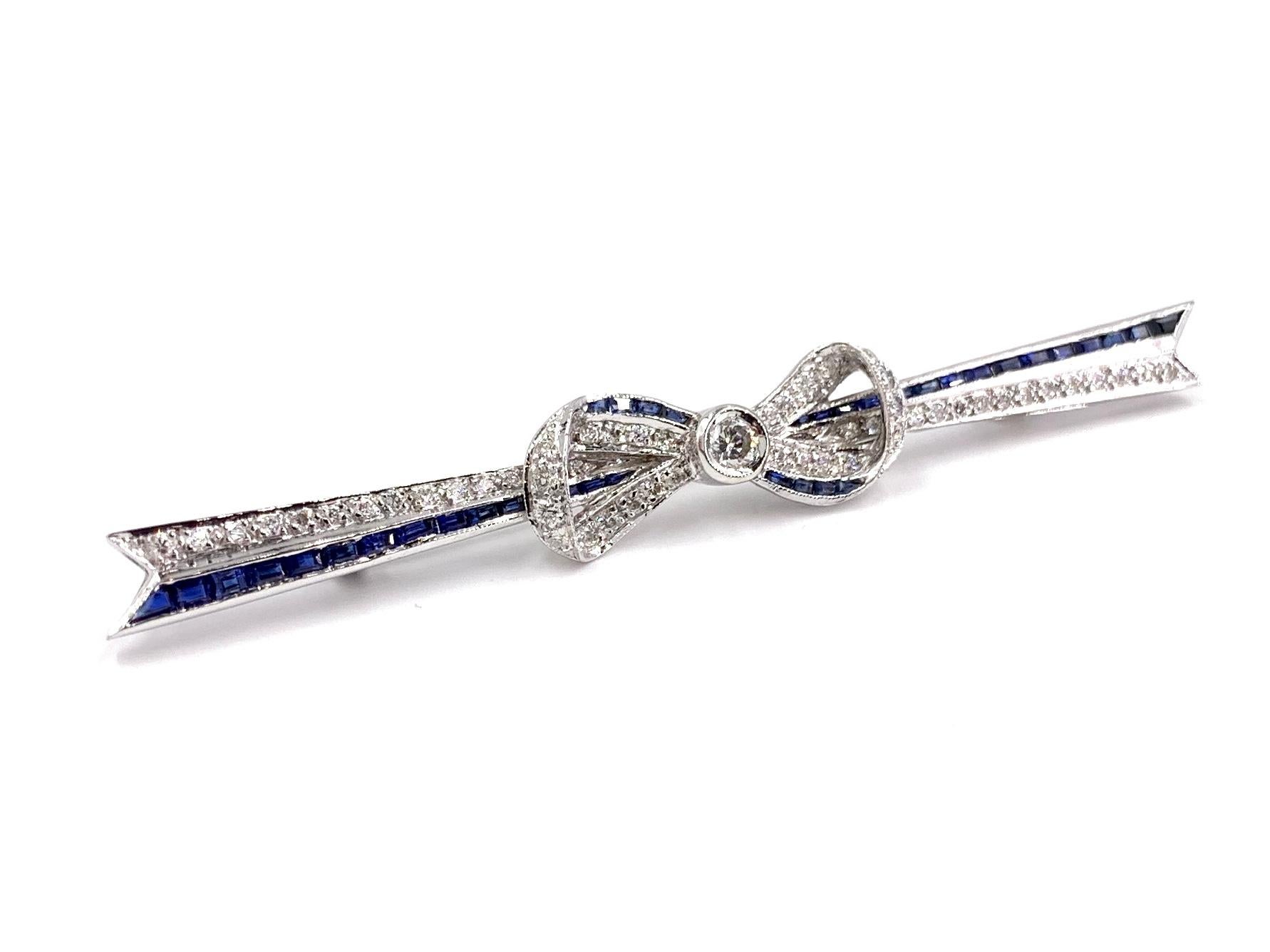 An Art Deco inspired 18 karat white gold horizontal bar style bow motif brooch featuring 2.33 carats of baguette cut blue sapphires and .60 carats of round brilliant white diamonds. Diamond quality is approximately G color, VS2 clarity. Brooch