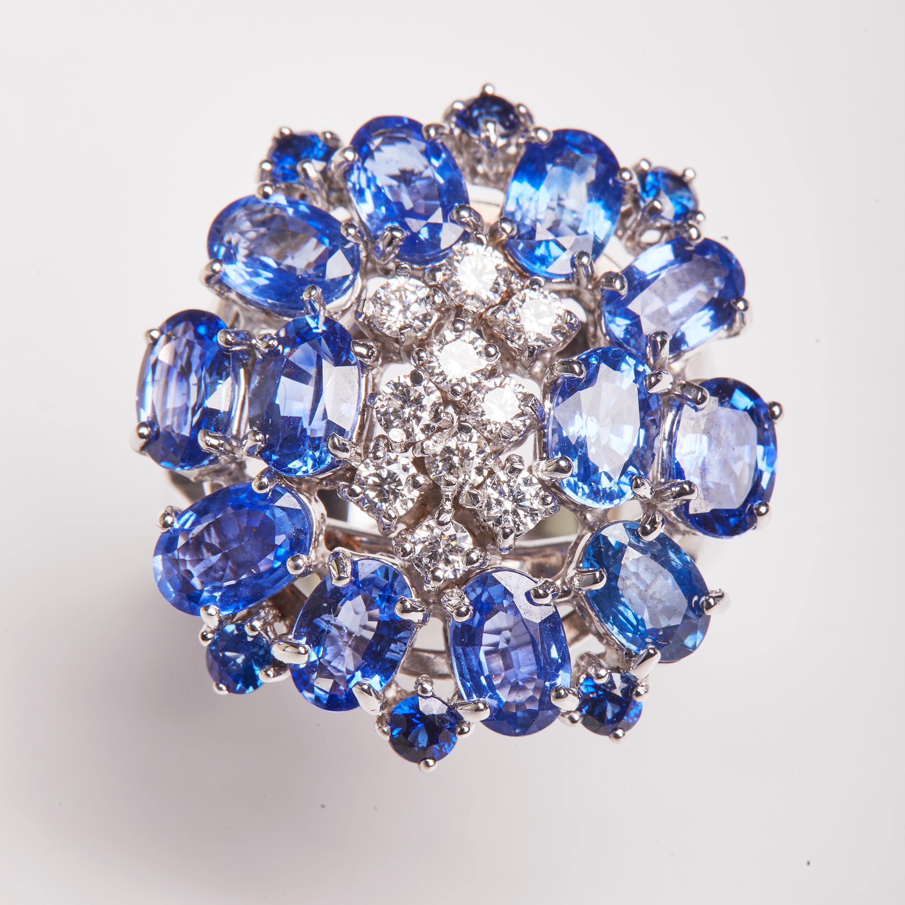 This 18 Karat White Gold Cocktail Ring features an outer layer oval cut Sapphire stones in a circular pattern, highlighting a midst of Diamonds. This exquisite ring would make a lovely pairing to our 18 Karat White Gold Sapphire And Diamond Dangle