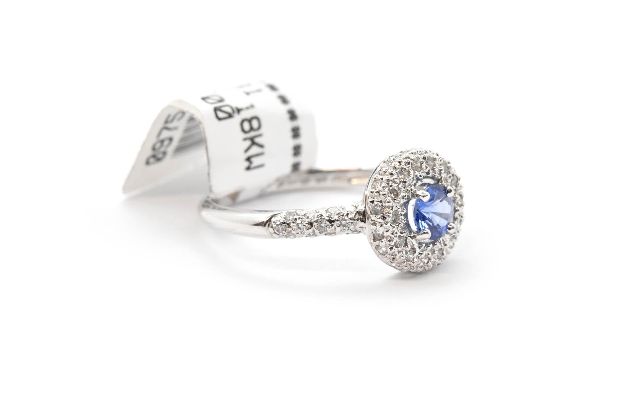 This fine fashion ring was designed in 18k white gold. The center stone of the ring is a lovely sapphire. This sapphire has a chilly shade of blue, and weighs 0.31ct. The sapphire has a lovely halo of diamonds around it, weighing 0.31cttw. There are