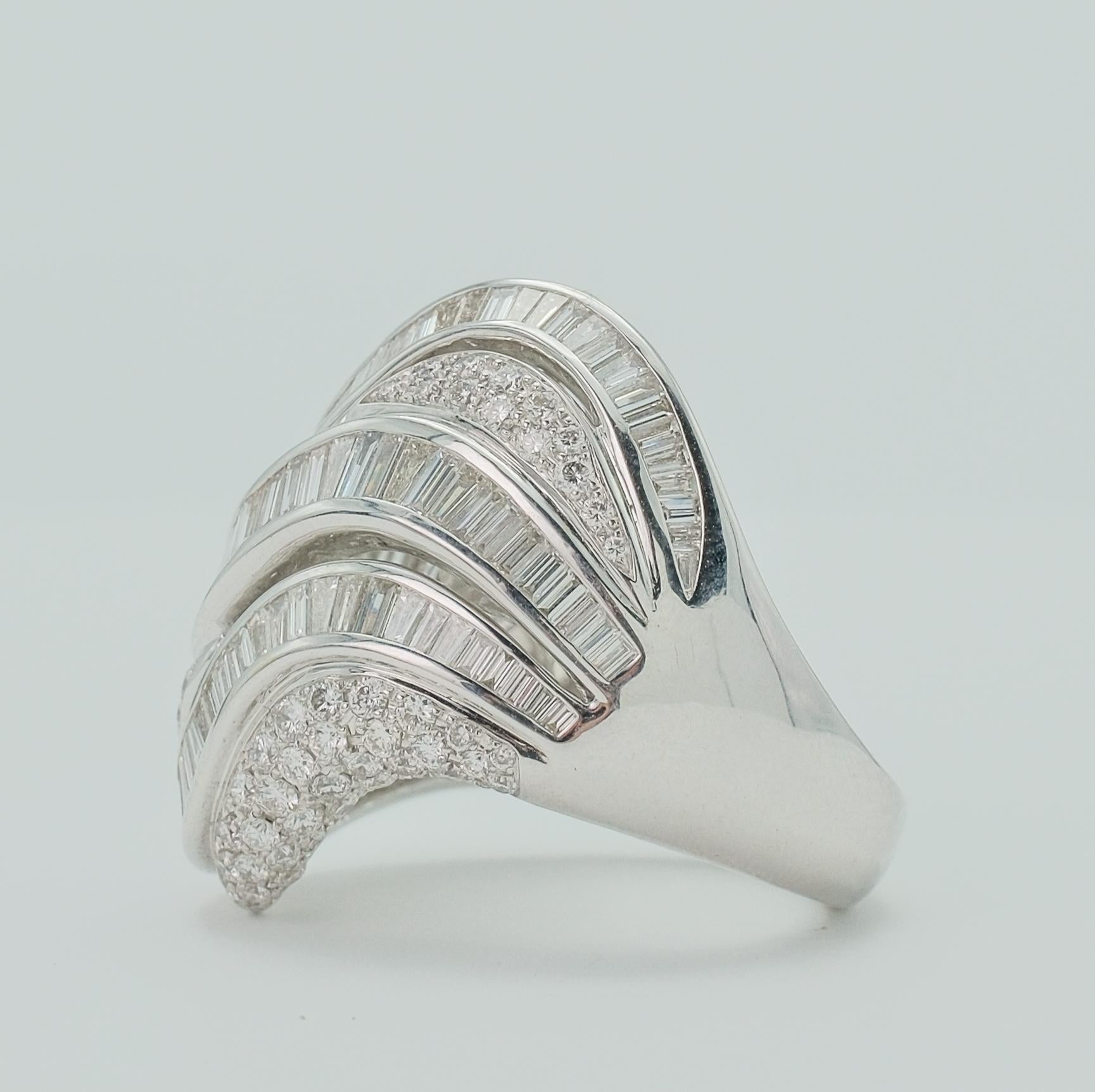 This exquisite 18k white gold diamond dome ring is a testament to expert craftsmanship. The ring features an intricate assembly of baguette and round-cut diamonds, each chosen for their stunning GH color and VS clarity. The gleaming band, crafted