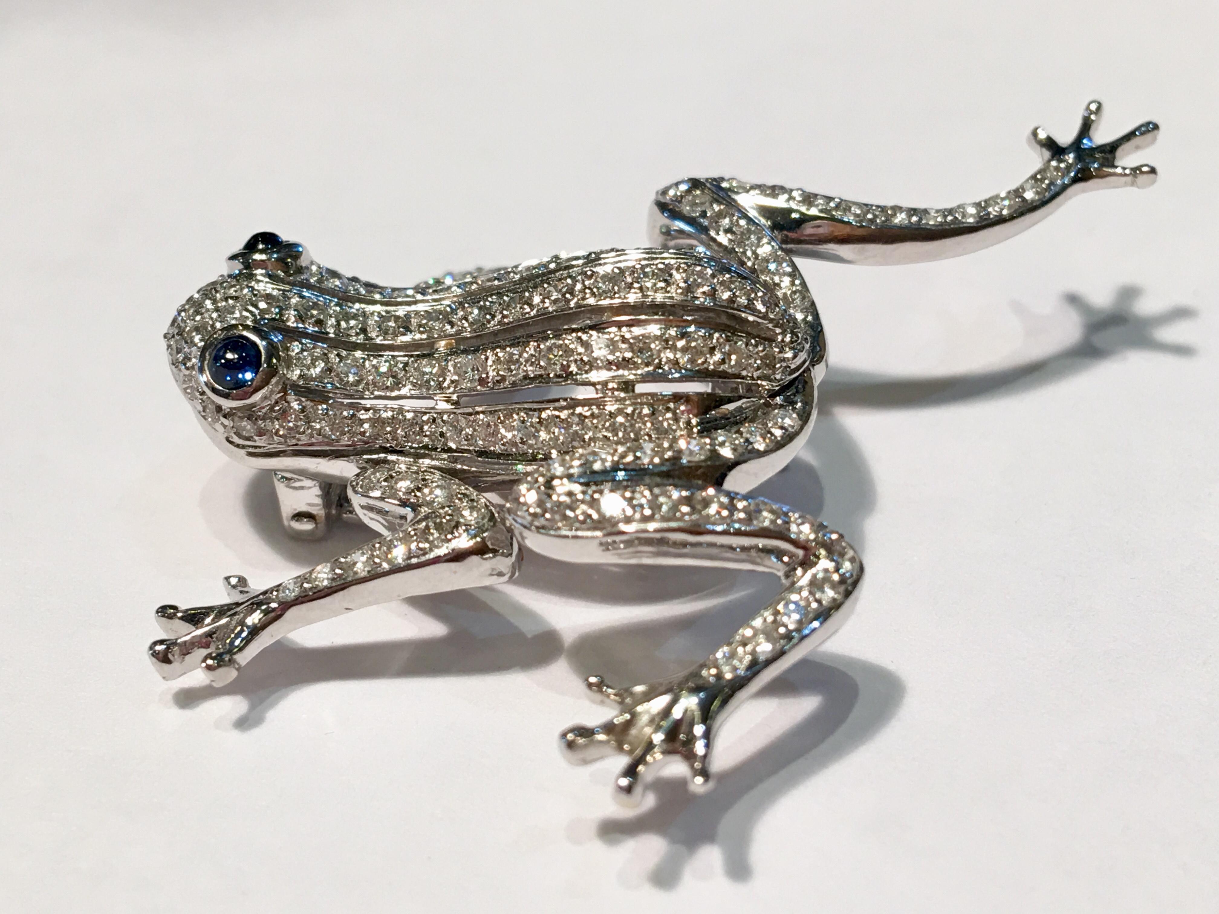 Contemporary 18 karat white gold brooch pin is a diamond frog with blue sapphire cabochon eyes and moving limbs.

Securely fastens with a double pin.

128 diamonds measure between 1 mm -  1.3 mm each and weigh approximately 1.5 carats total diamond