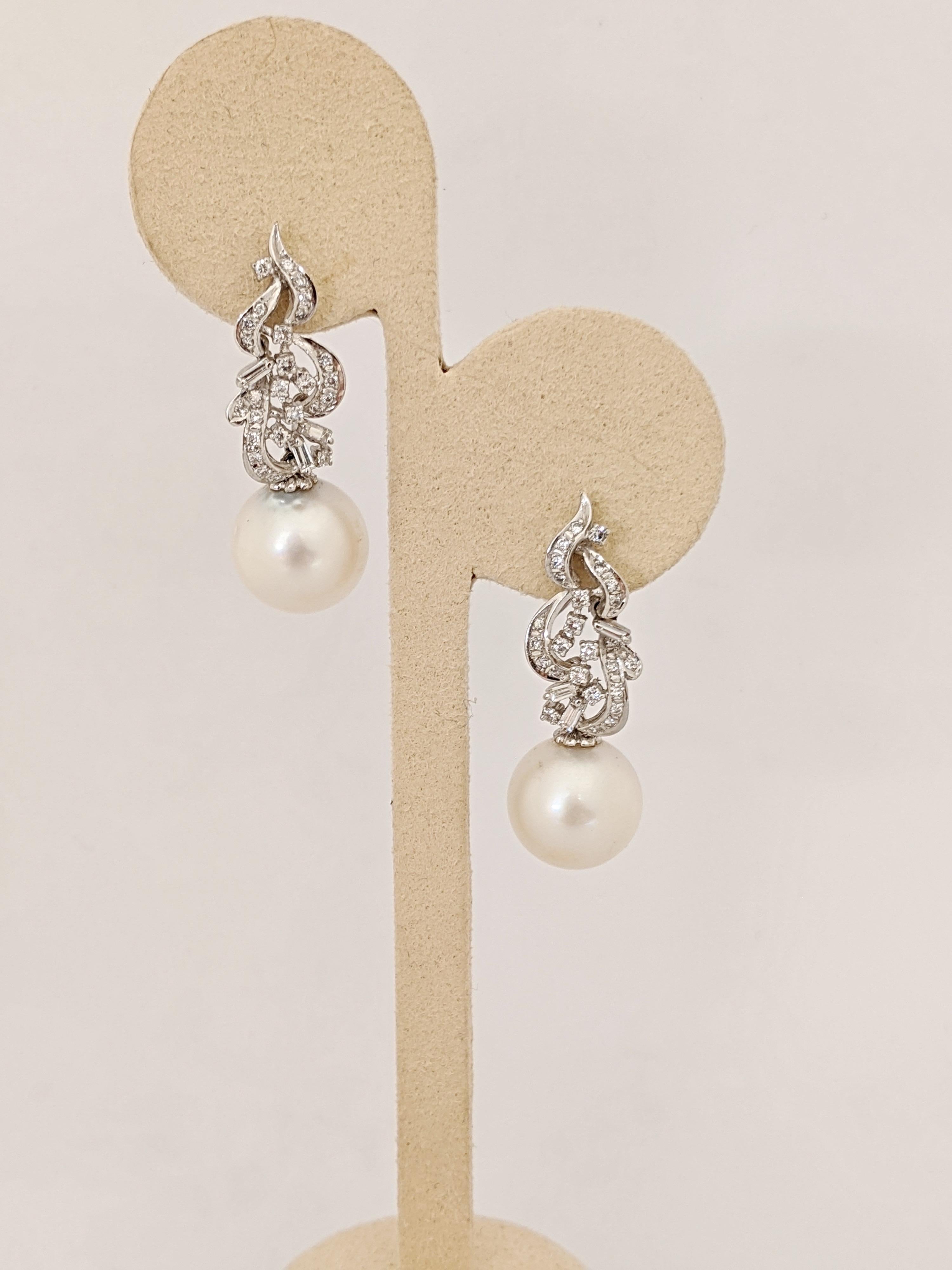 A pair of 18 karat white gold and Diamond hanging earrings with a South Sea Pearl drop. The top part of the earrings are designed with a swirly shape set with round brilliant and baguette cut Diamonds. South Sea Pearls 13.3mm x 13.2 mm hang below