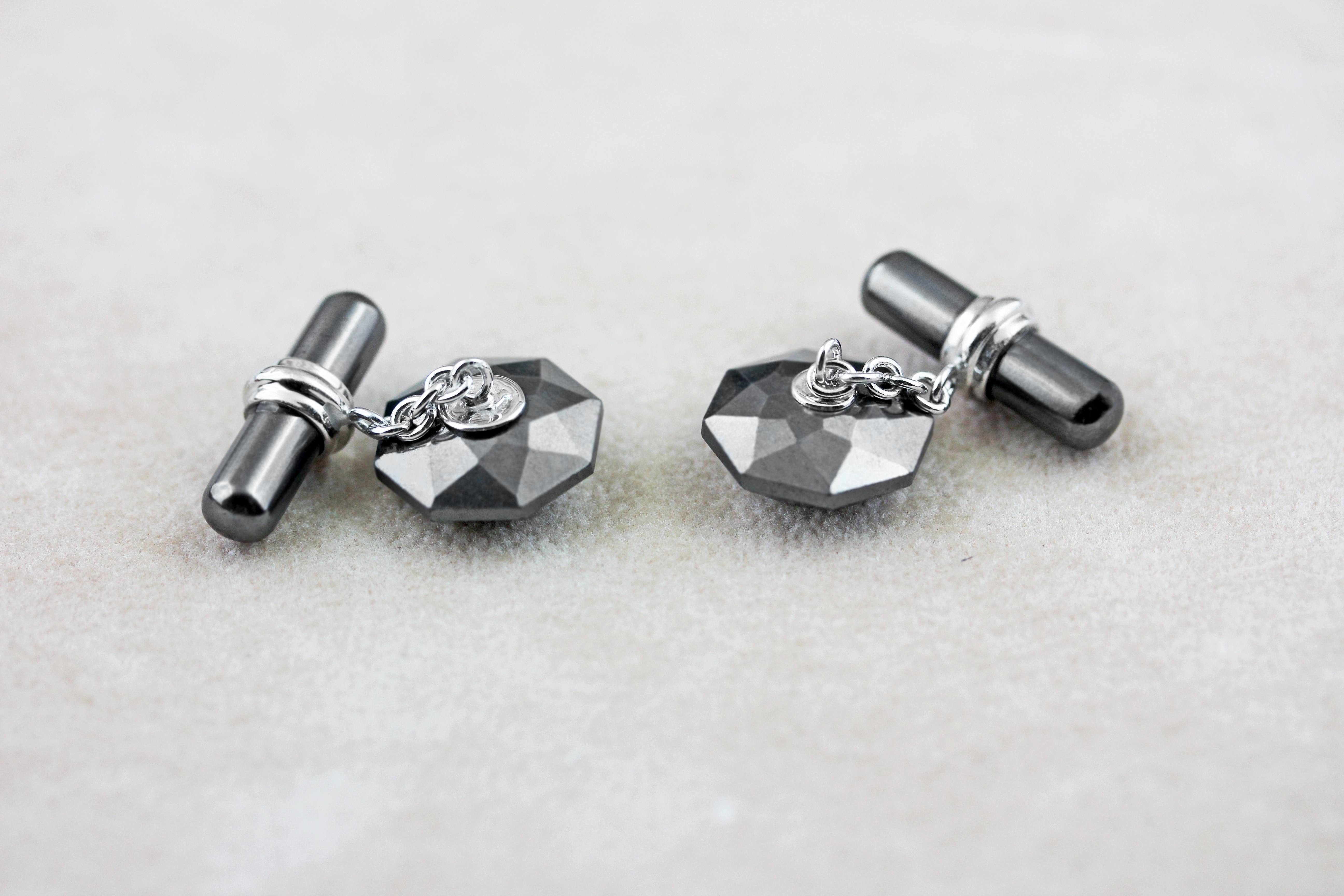 The striking black shade of hematite gives the classic design of these cufflinks a modern edge. 
The front face is shaped as a convex octagon, whose many cuts beautifully reflect light, while the center is adorned with a cabochon emerald. 
The