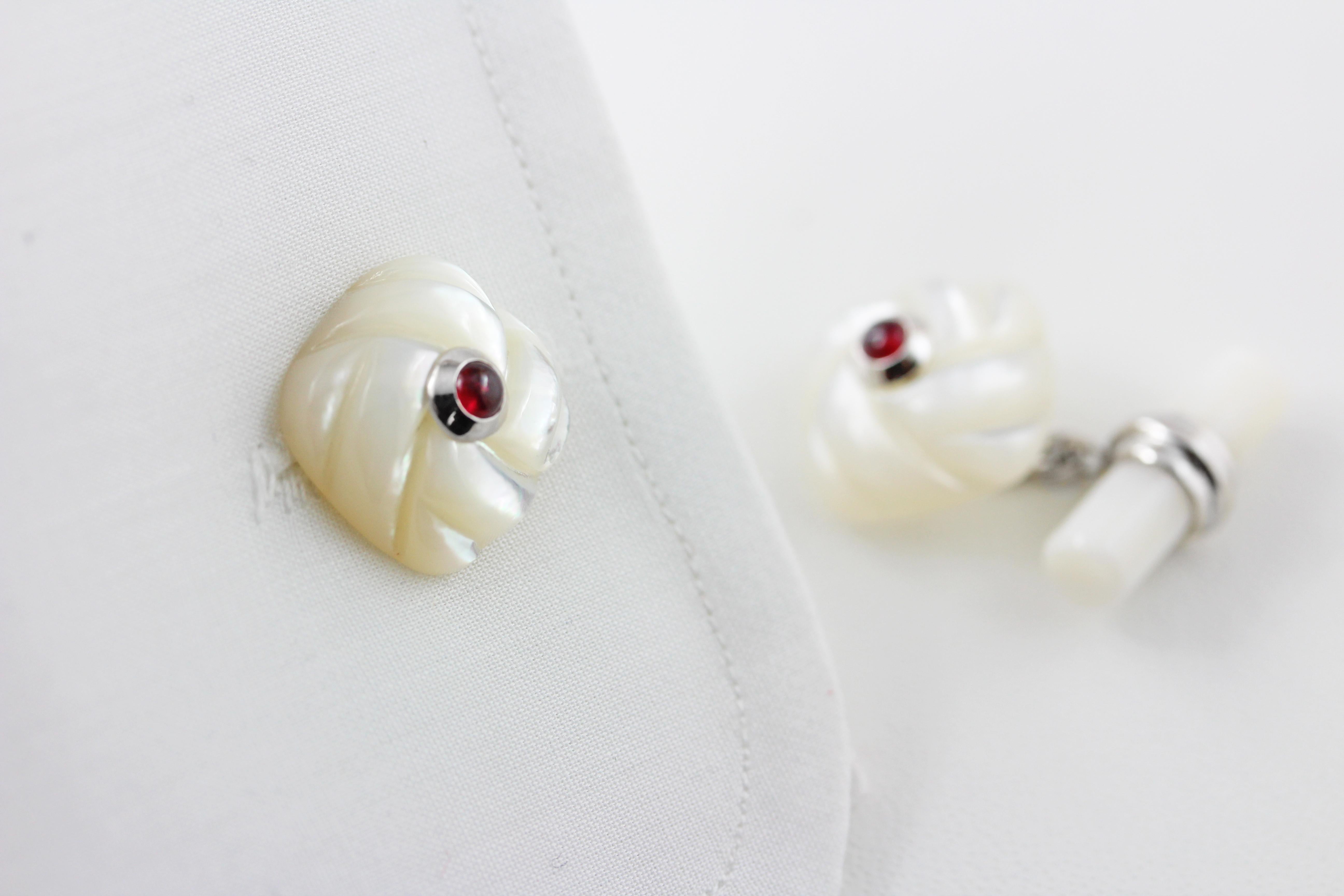 These classic cufflinks are made of mother of pearl and feature a front face shaped as a square with a striking texture that mimics an interwoven fabric. 
The squares are adorned in the center with cabochon ruby. 
The toggle is  a simple cylinder