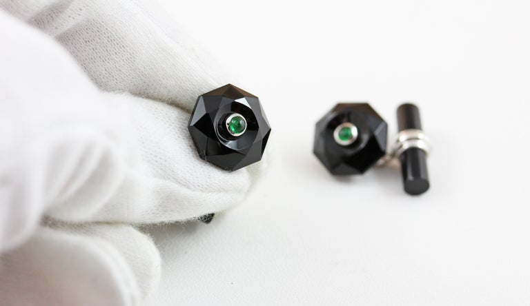 The front face of these exquisite cufflinks has a striking octagonal shape that is convex, multifaceted, and adorned in the center with a cabochon emerald. 
Both the front face and the cylindrical toggle are in onyx, with a post made of 18 karat