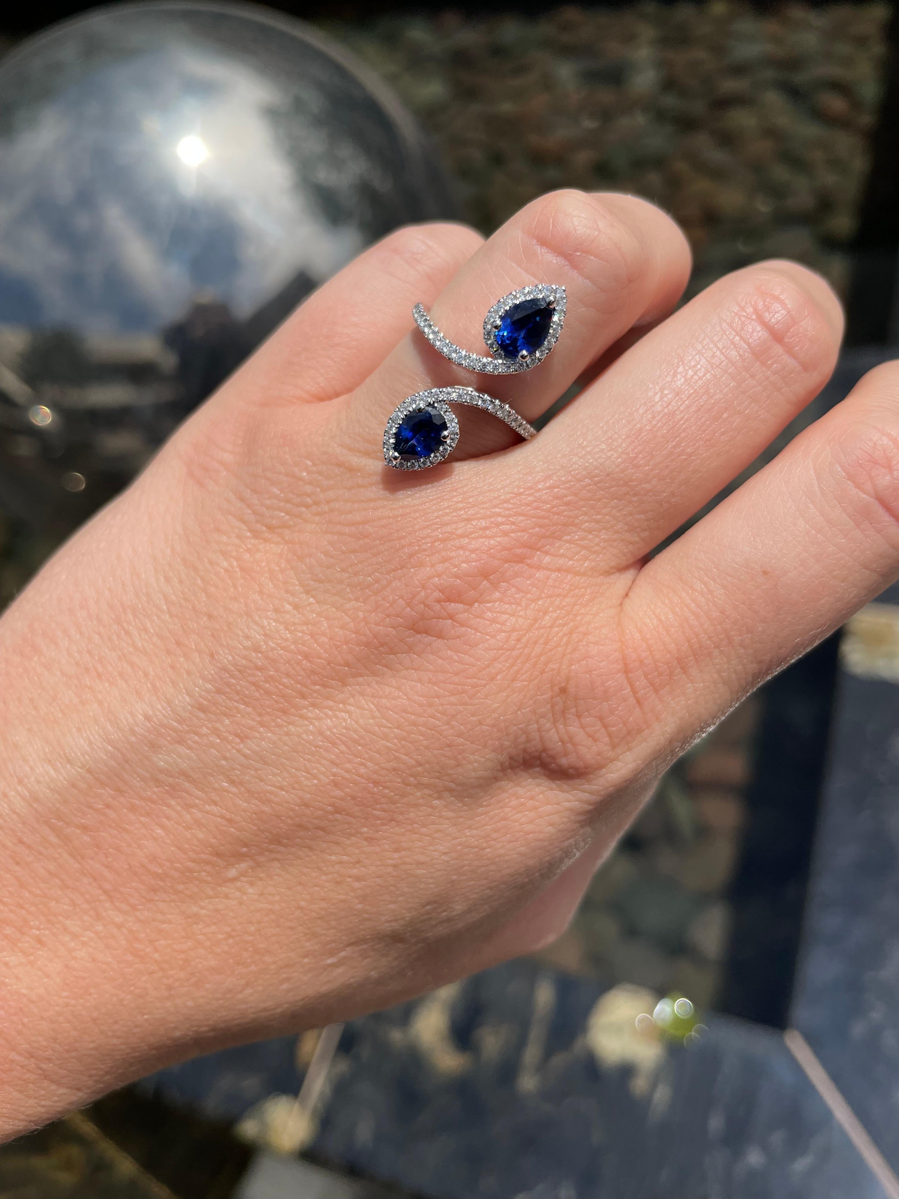 18 karat white gold bypass ring with 2 pear shape blue sapphires weighing a carat total weight of 1.65 carats and 66 round brilliant cut diamonds totaling 0.38 carat total weight.