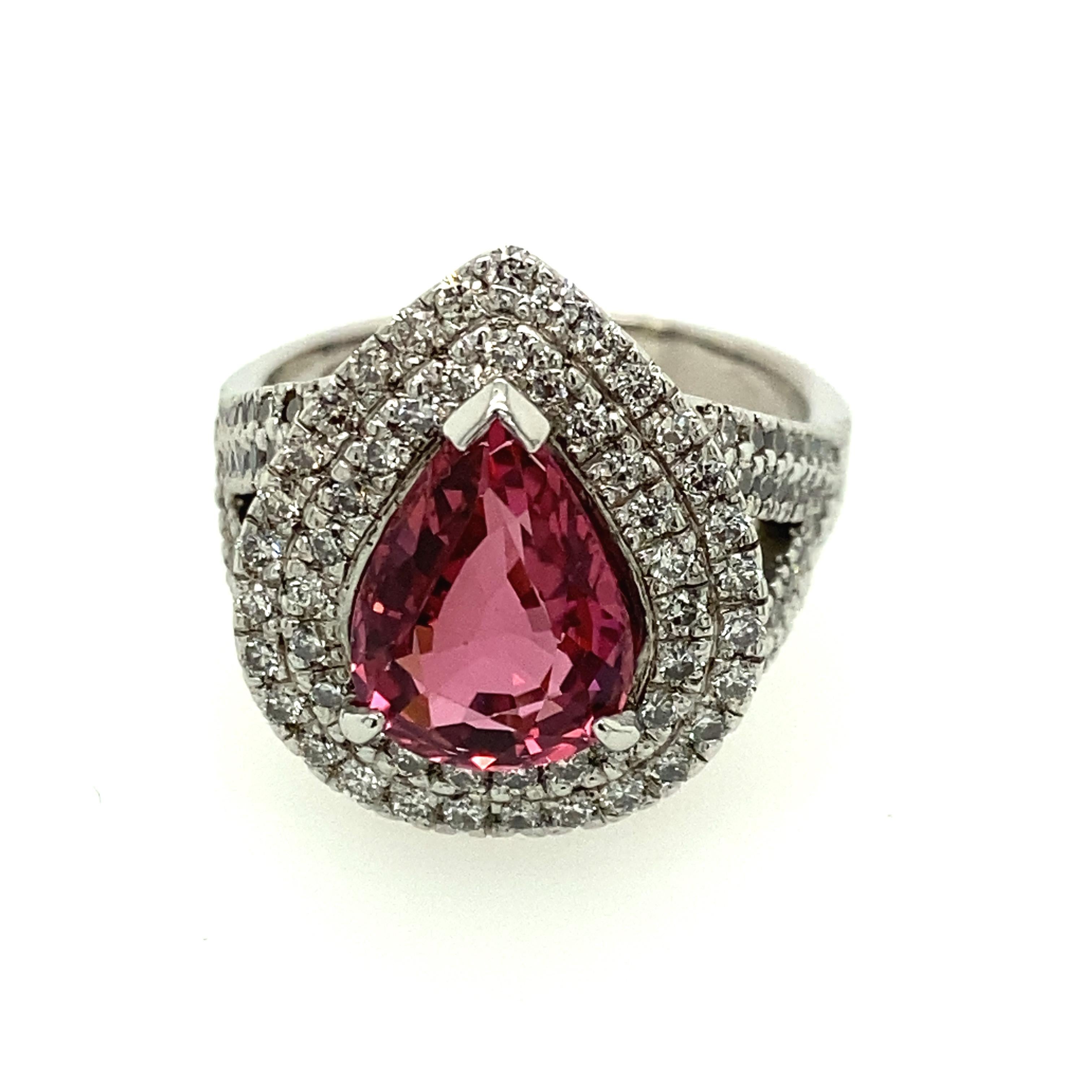 18 Karat White Gold Pink Tourmaline Diamond Ring.
The center stone is a pear shape pink tourmaline secured in a three claw setting. Surrounding the pink tourmaline is two rows of diamonds forming a pear shaped cluster head. Two split top shoulders