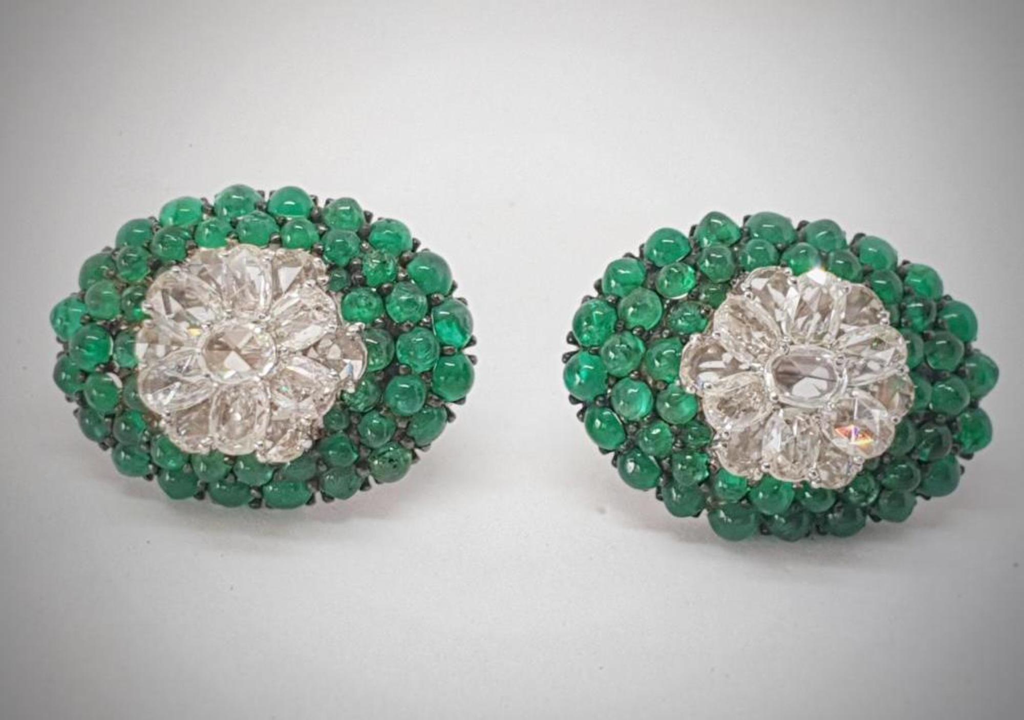 Round natural emerald cabochons are prong set along with layers of oval shape rose cut diamonds in these ear studs which resemble an oval sugar loaf. The area where the emeralds are set is plated in black colour. We, as a design house have been