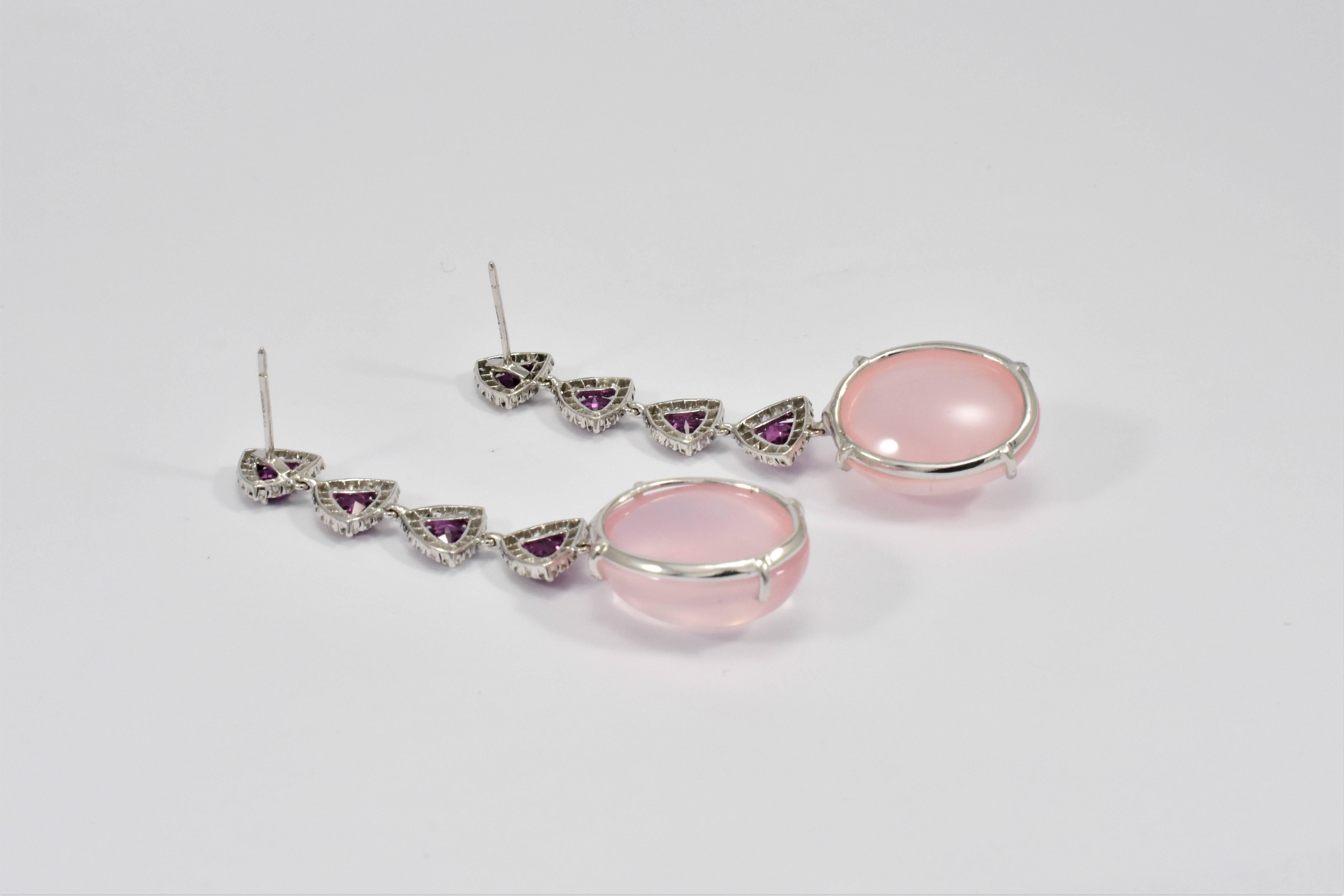 A lovely and eye catching pair of swinging ear pendants in 18ct white gold and pink mauve tones. The line of earring drops is formed of four bright purple garnet trilliant cut faceted stones each framed by a border of diamonds and linked to each